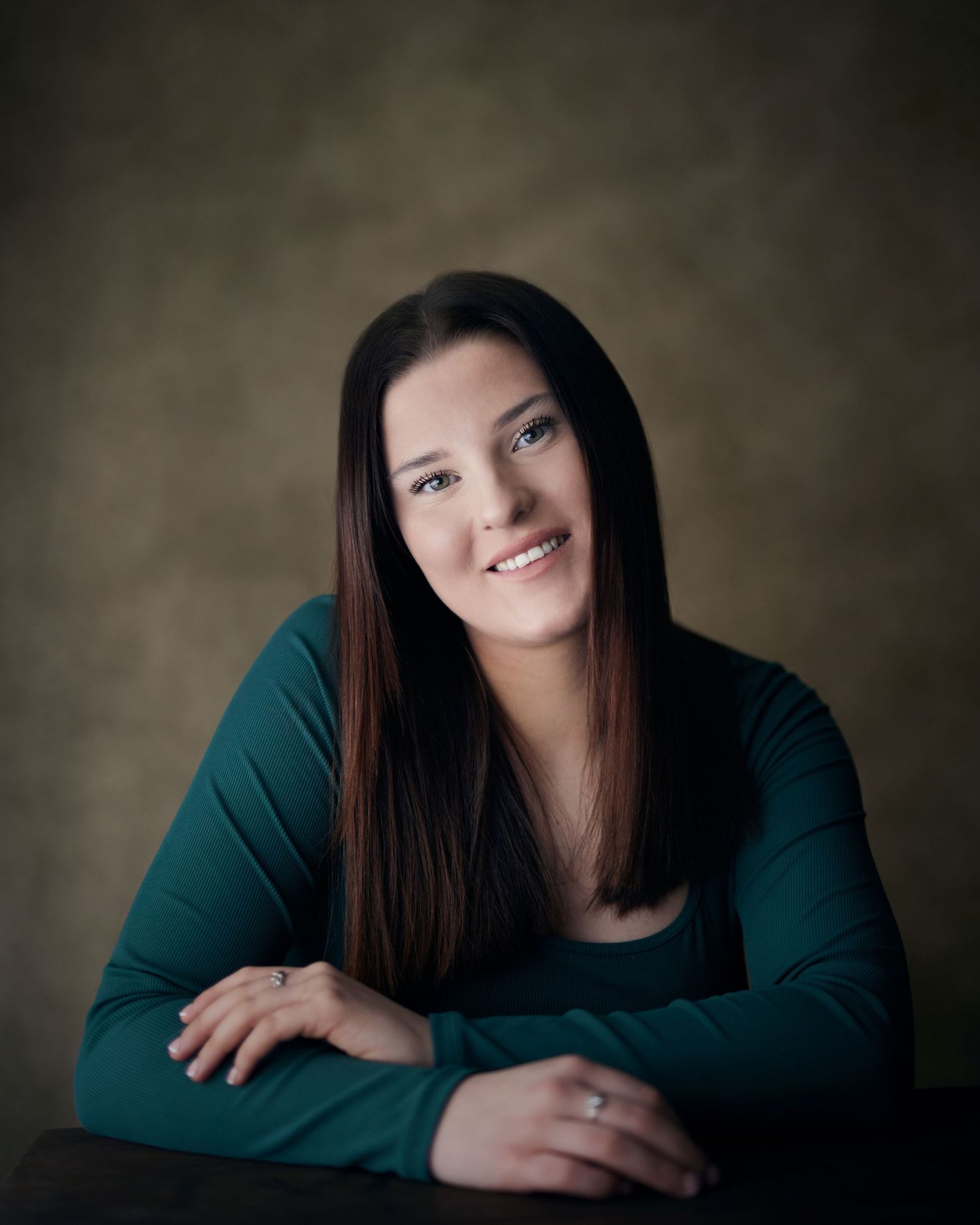 Friendly headshot; woman with a natural smile and soft studio lighting against a brwon canvas backdrop.