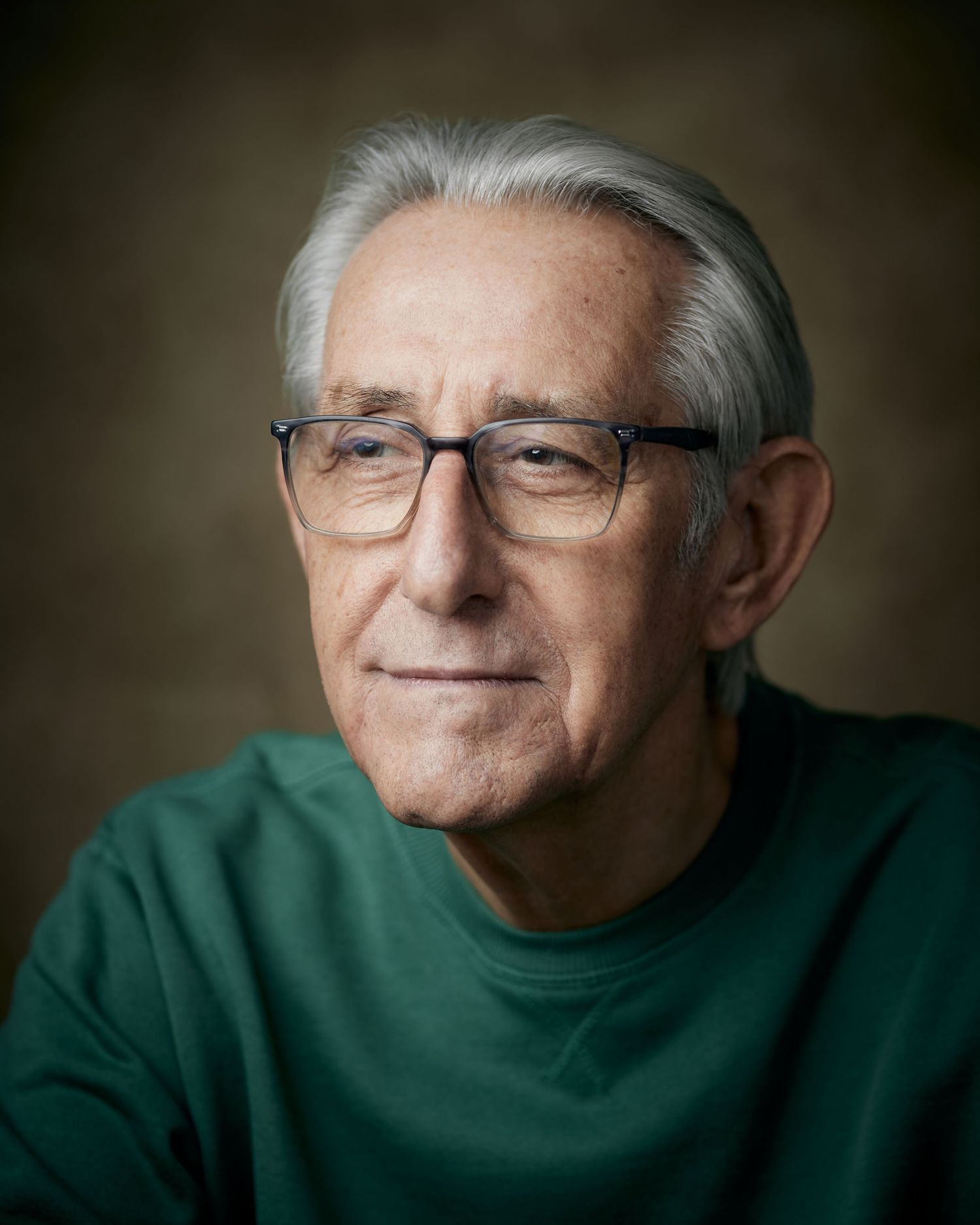 Soulful classic headshot; man with a contemplative gaze looking off-camera against a brown canvas backdrop.