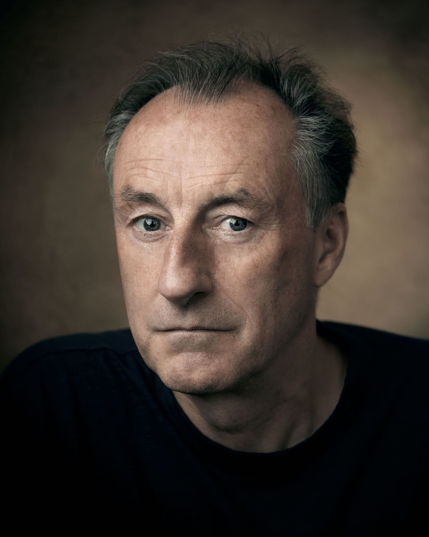 Intense studio headshot of a male actor with a knowing look in his eyes.