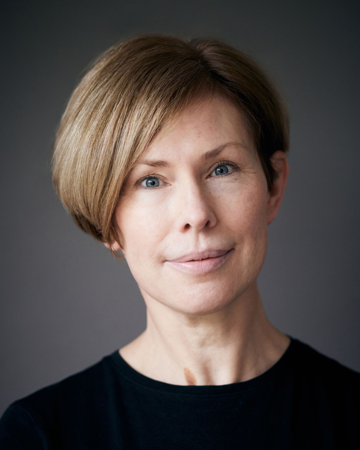 Natural professional portrait by Director Geraint Todd; woman with a calm, approachable gaze on a grey background.