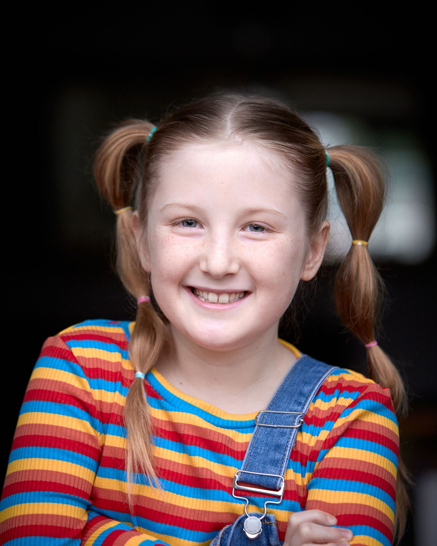 Bright, cheerful child actor headshot. Red pigtails, striped shirt, and denim. High-energy, approachable look for commercial TV casting.