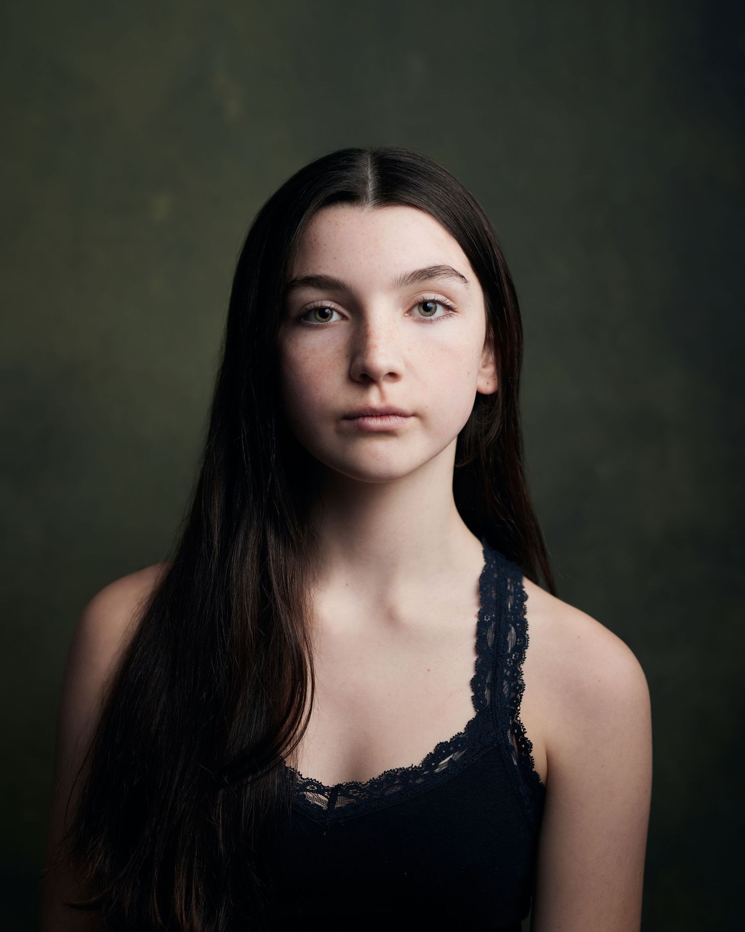 Formal studio portrait; young girl with a vintage-inspired aesthetic on a green backdrop.