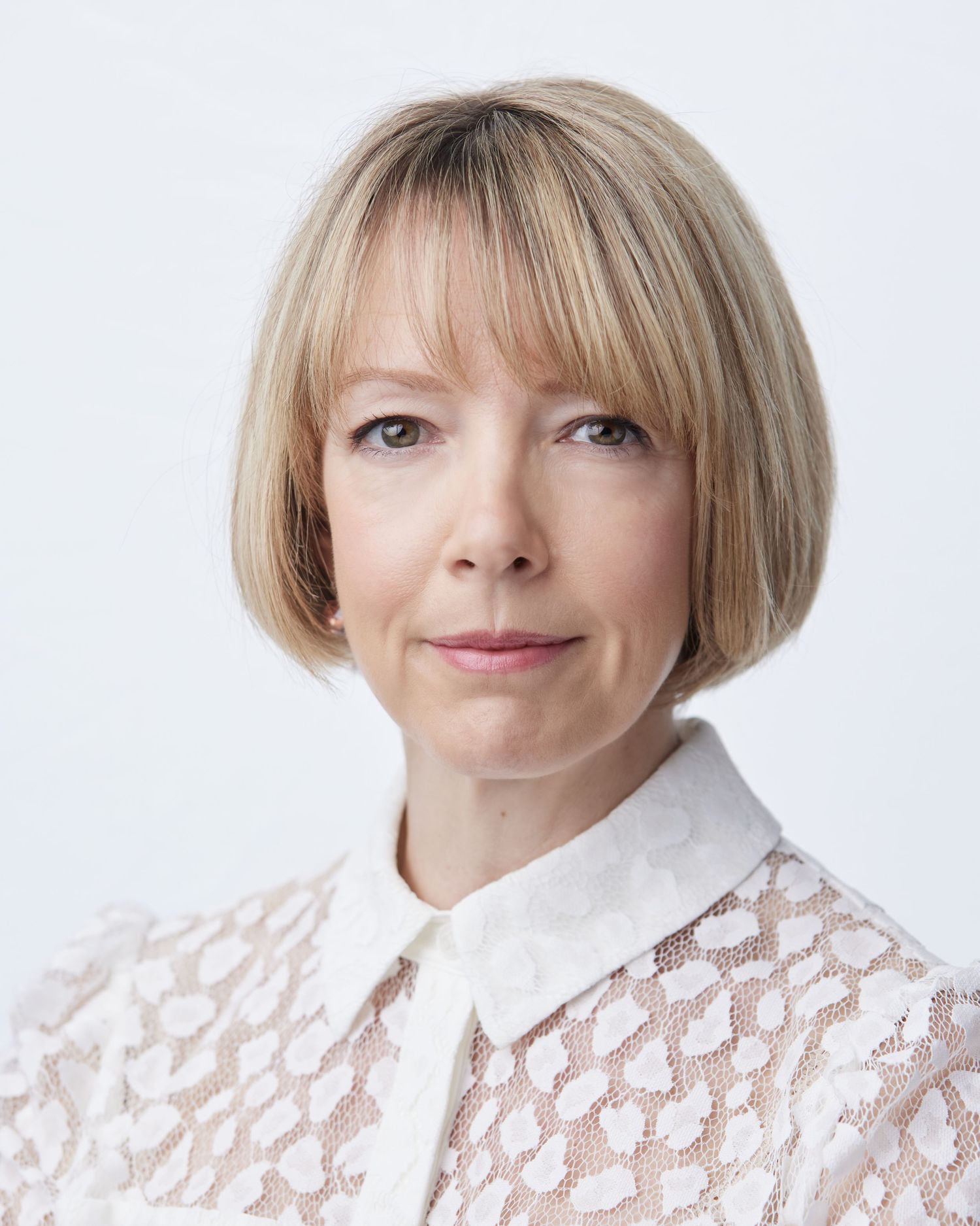 Professional business headshot by Director Geraint Todd; woman with a white lace shirt, offering a calm, confident gaze on a white backdrop.
