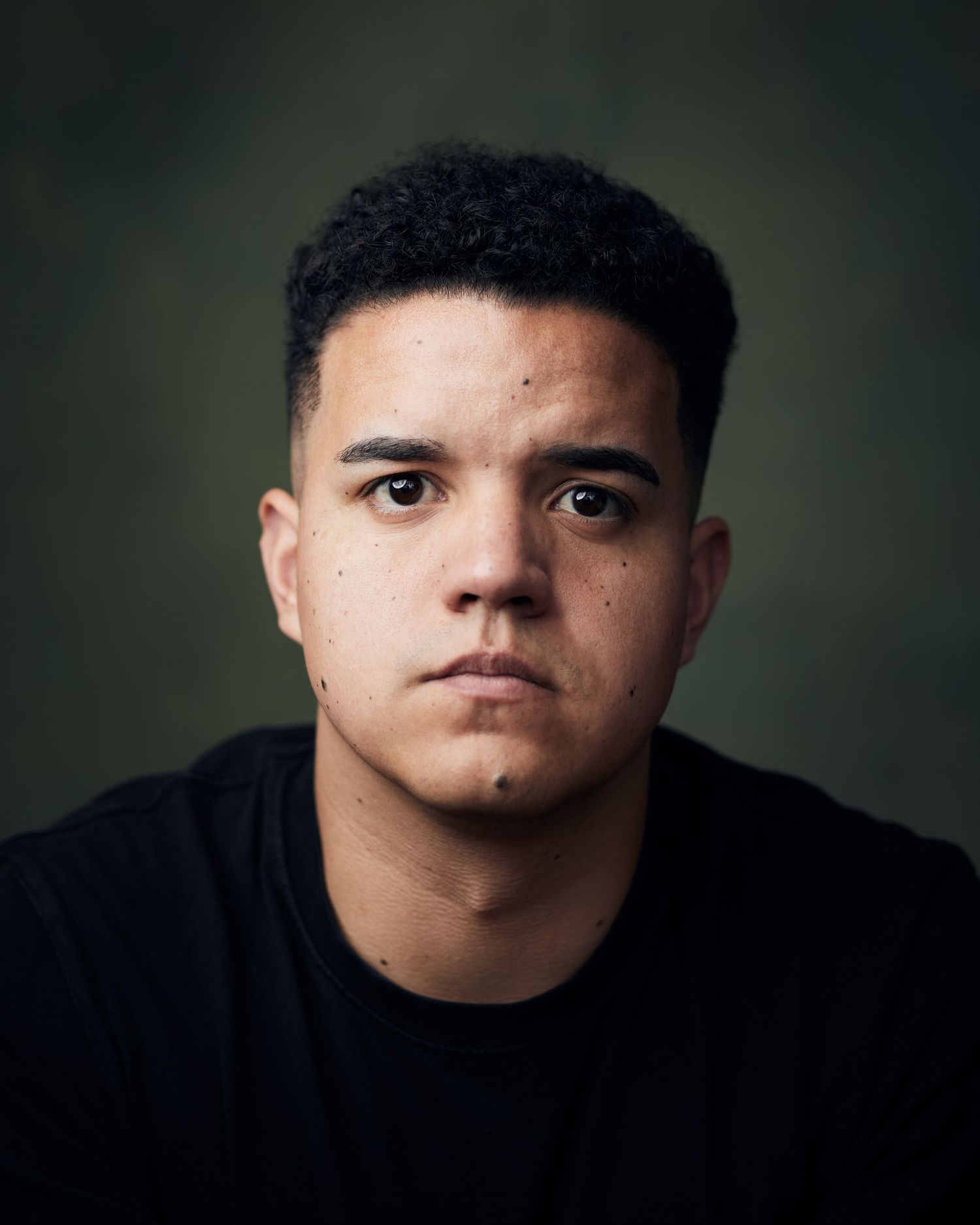 Intense dramatic headshots male actor with a moody, defiant gaze against a green background.