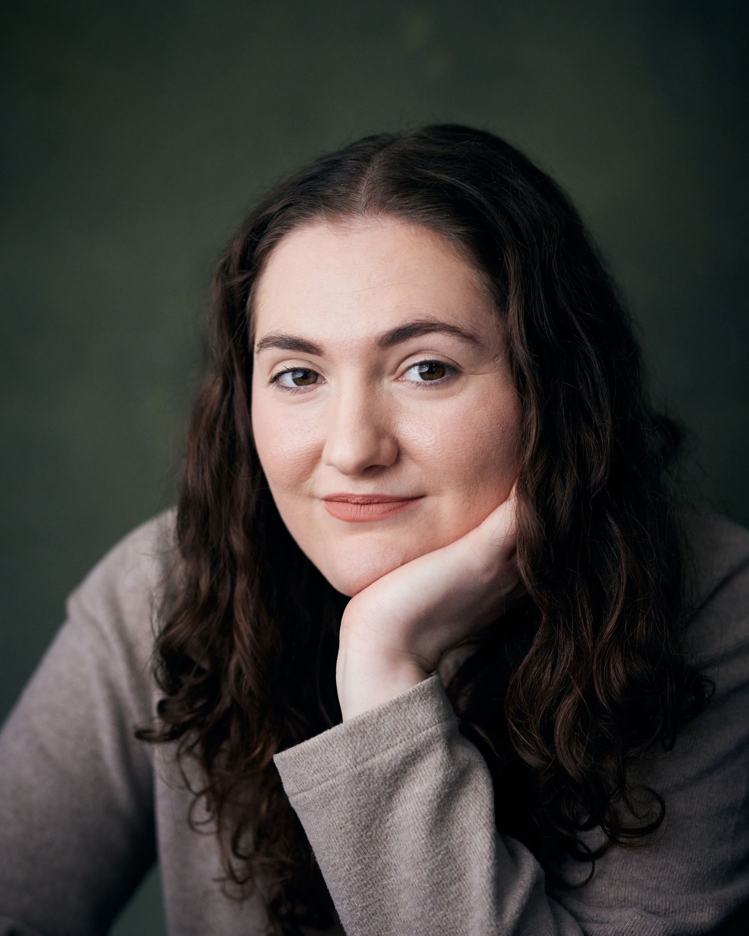 Actor headshot by Geraint Todd; woman with a warm, open smile and soft lighting against a textured green backdrop.