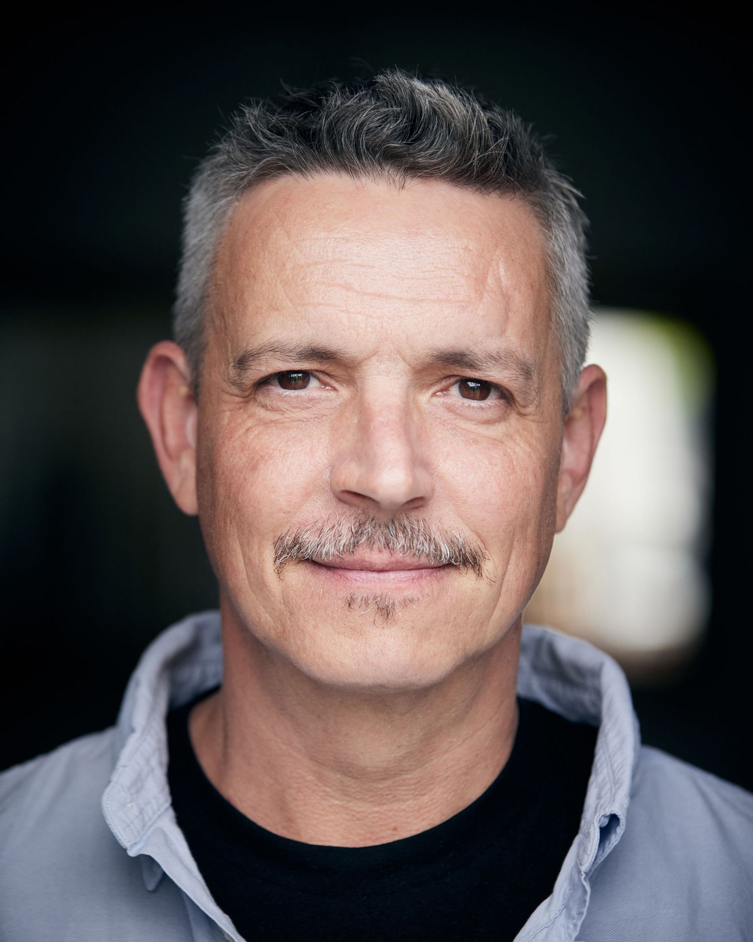 Likeable character portrait; approachable gaze with soft-lit Cardiff background.