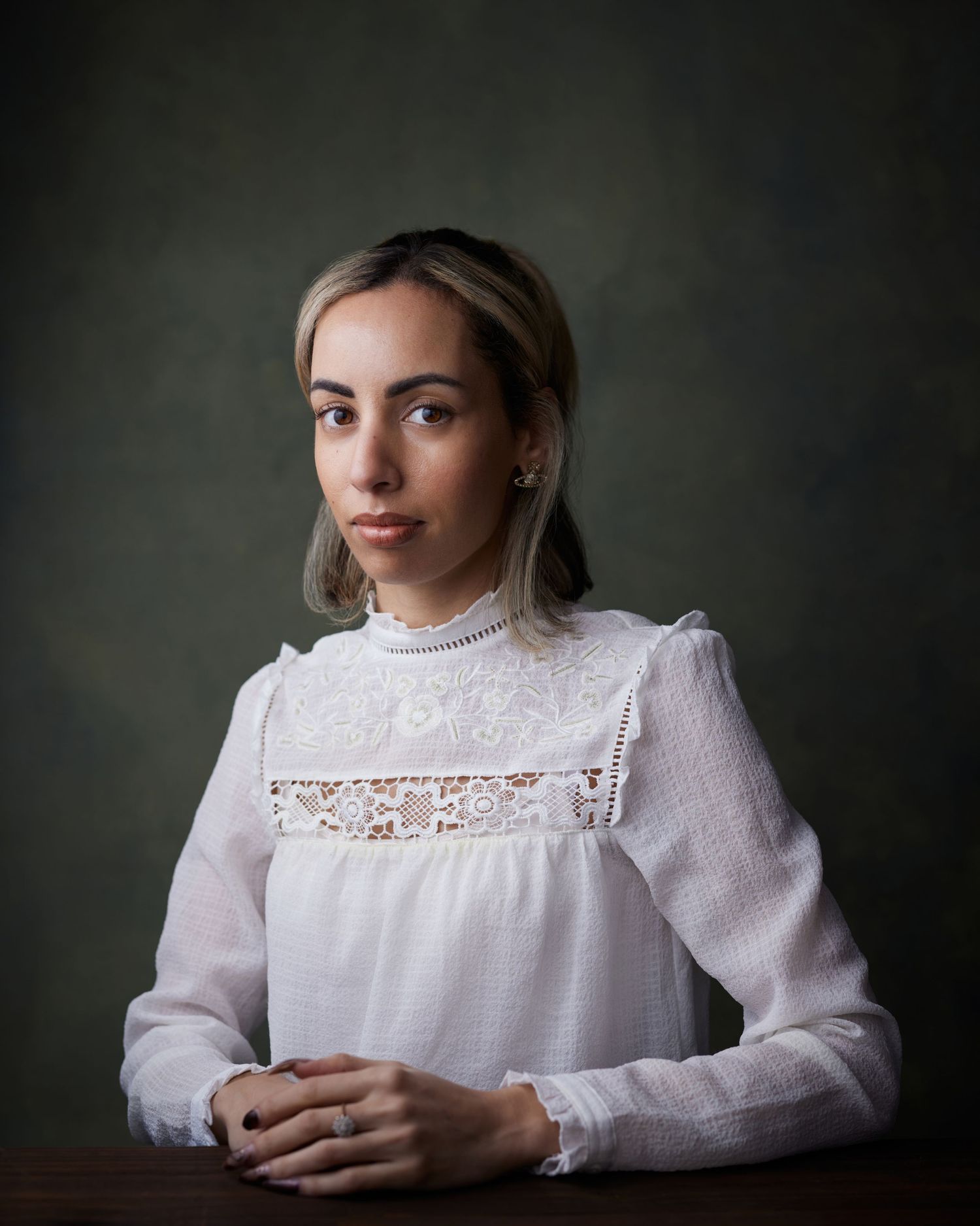 Classic studio portrait; woman with a thoughtful, poetic gaze against a deep green backdrop.