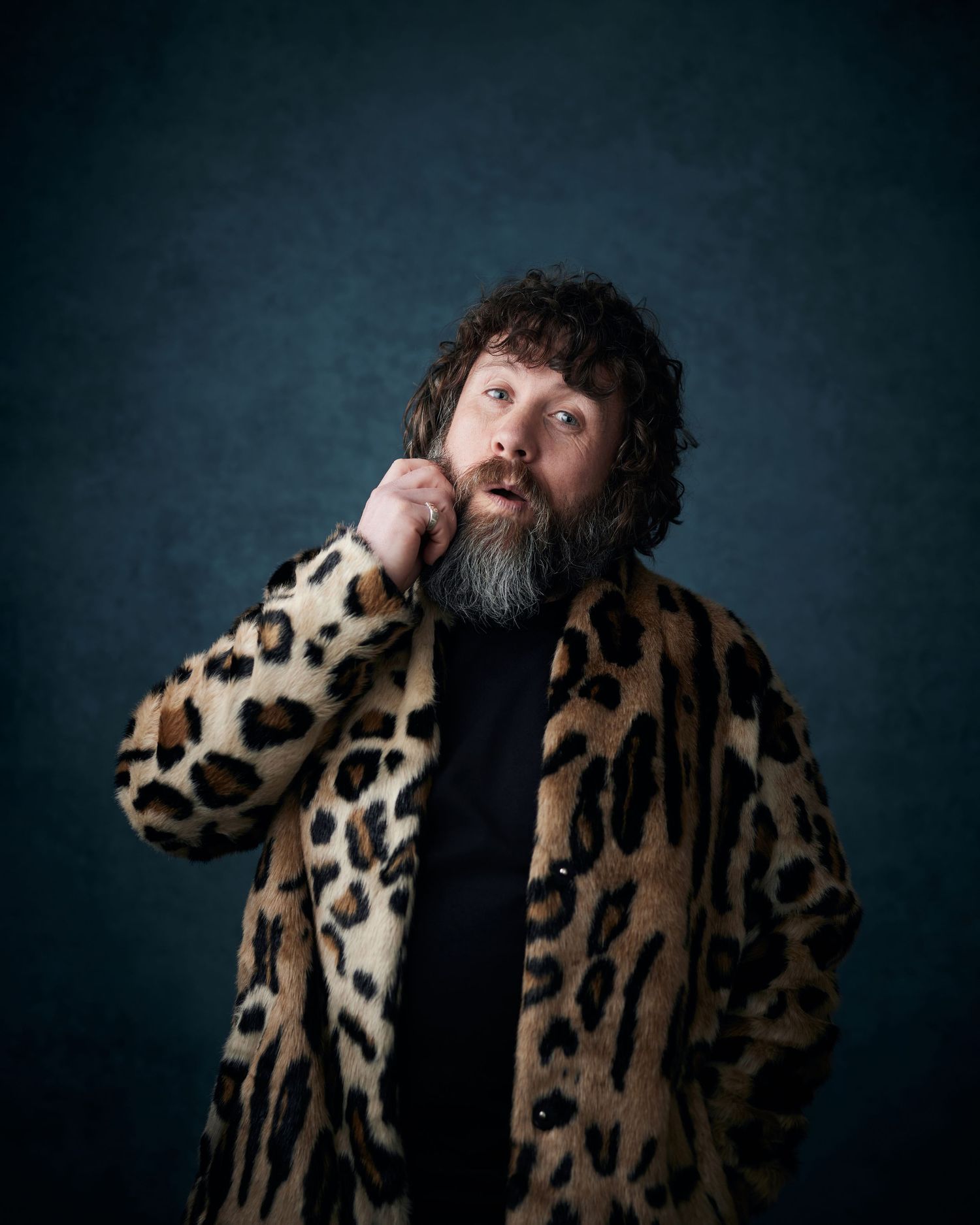 Upbeat headshot; male actor with a friendly and engaging look in a leopard-print coat against a blue backdrop.
