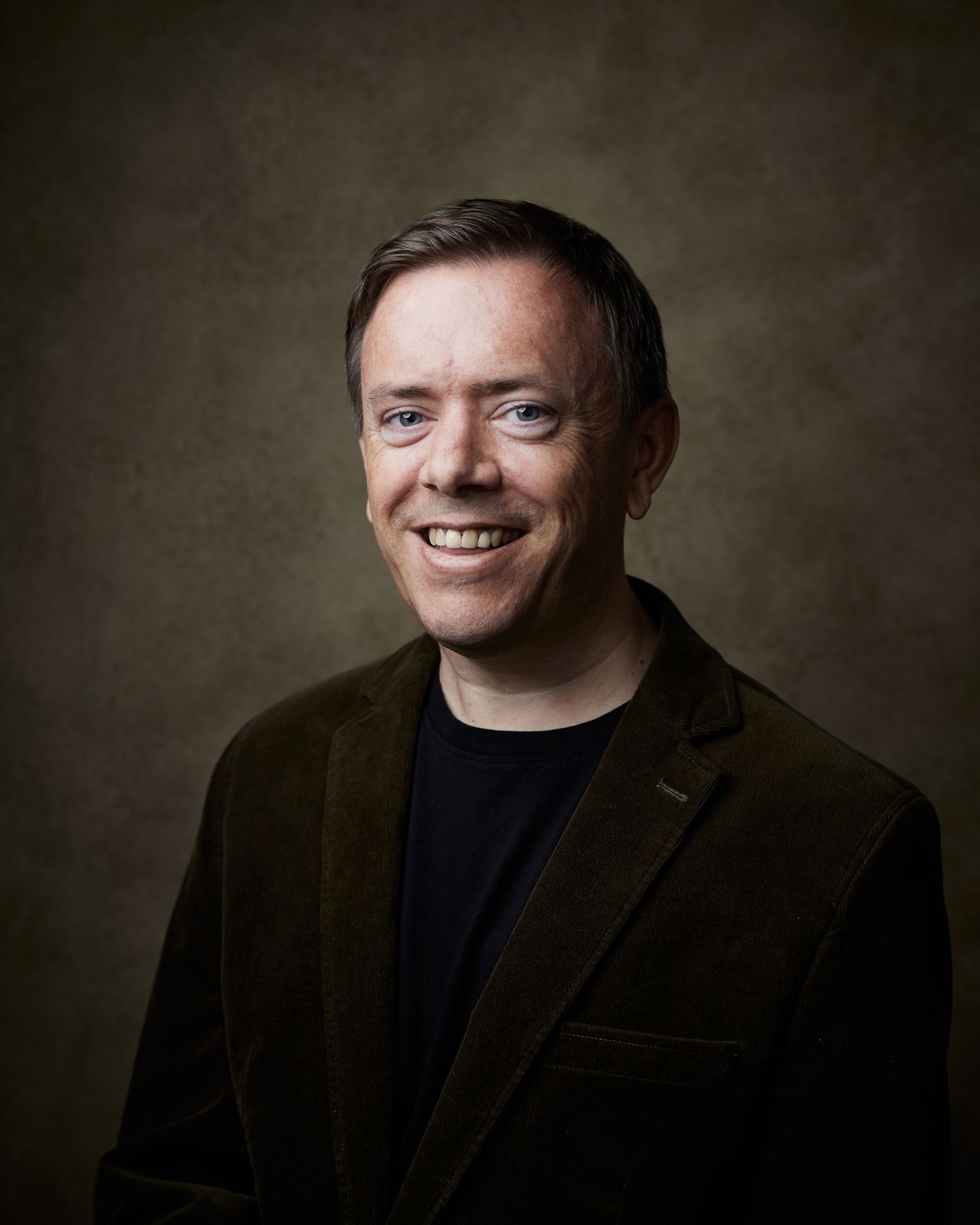 Positive-energy portrait; male performer with a bright and joyful smile against a brown canvas backdrop.