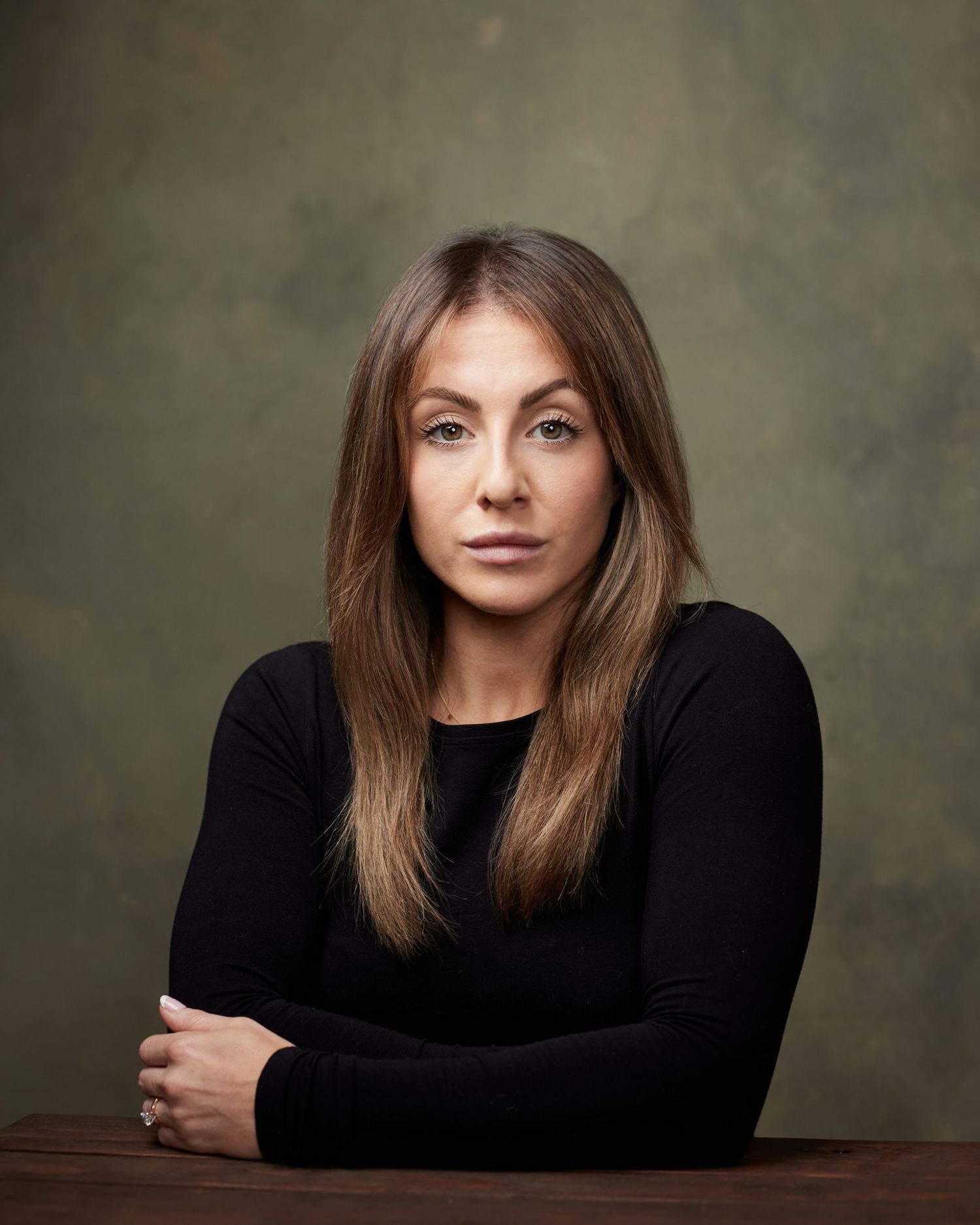 Dramatic actor headshot; woman with a strong, defiant, serious gaze against a dark green textured backdrop.