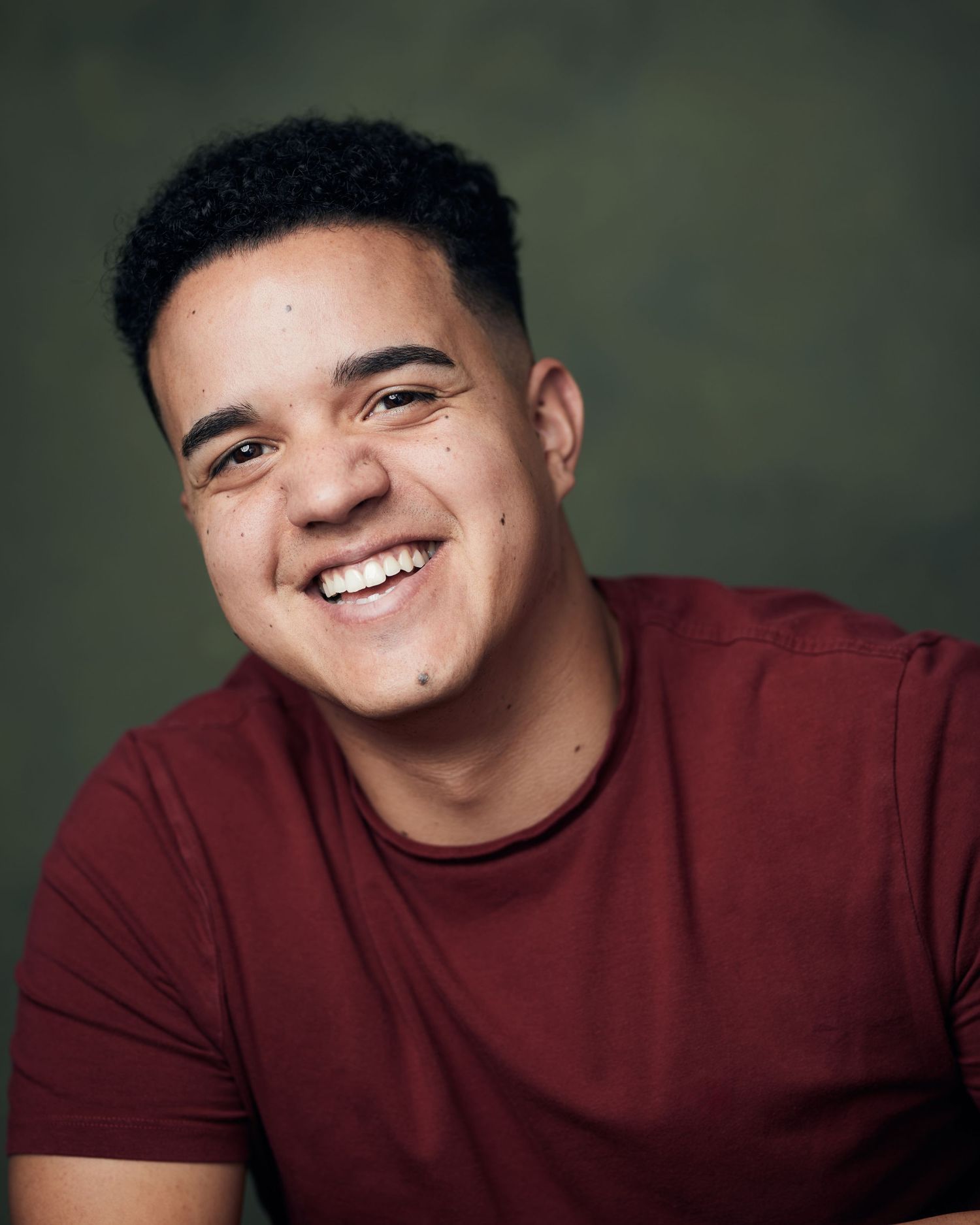 Engaging studio portrait; male performer with a bright, high-energy presence against a green canvas backdrop.