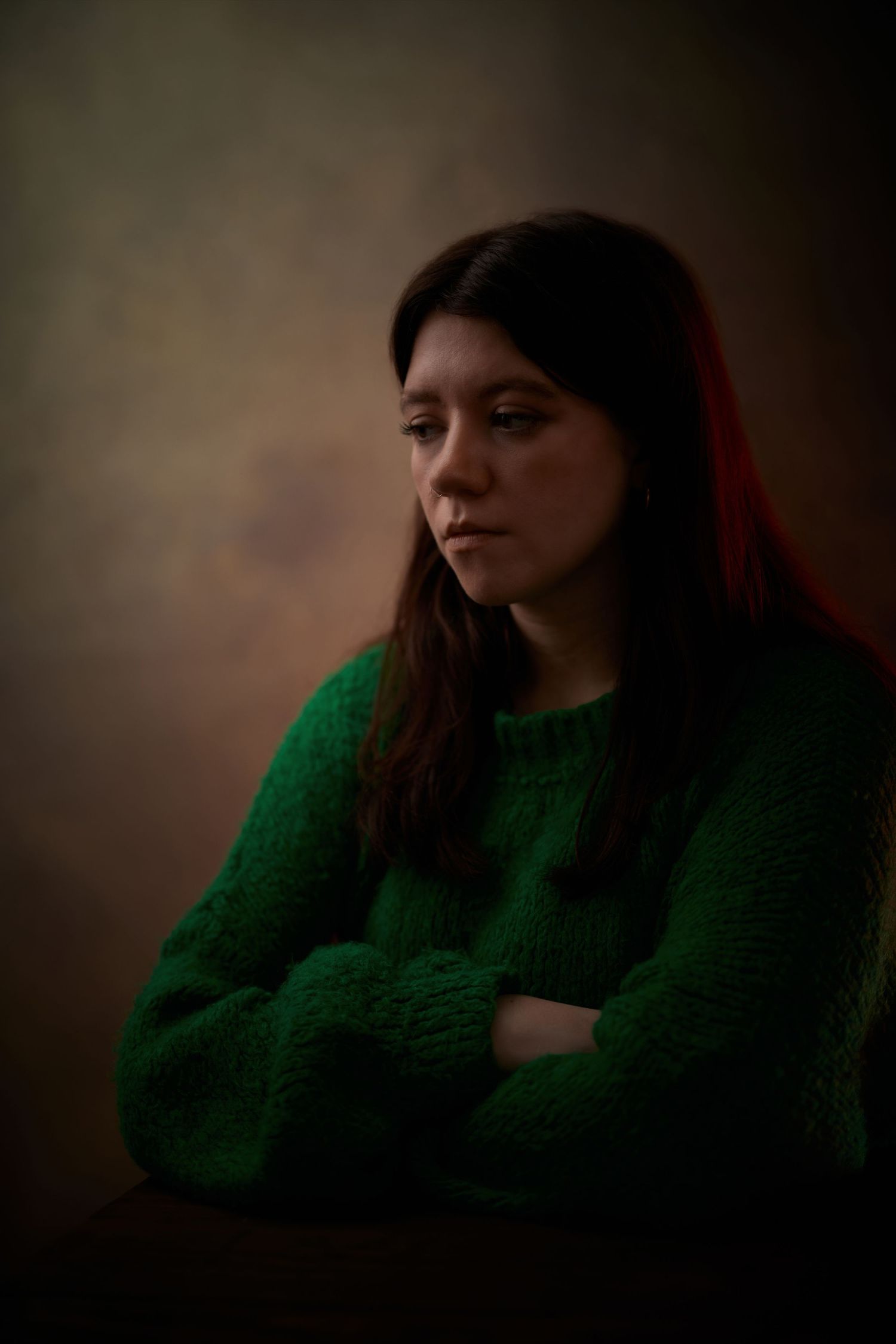 Cinematic portrait; woman with a contemplative gaze on a deep brown backdrop.