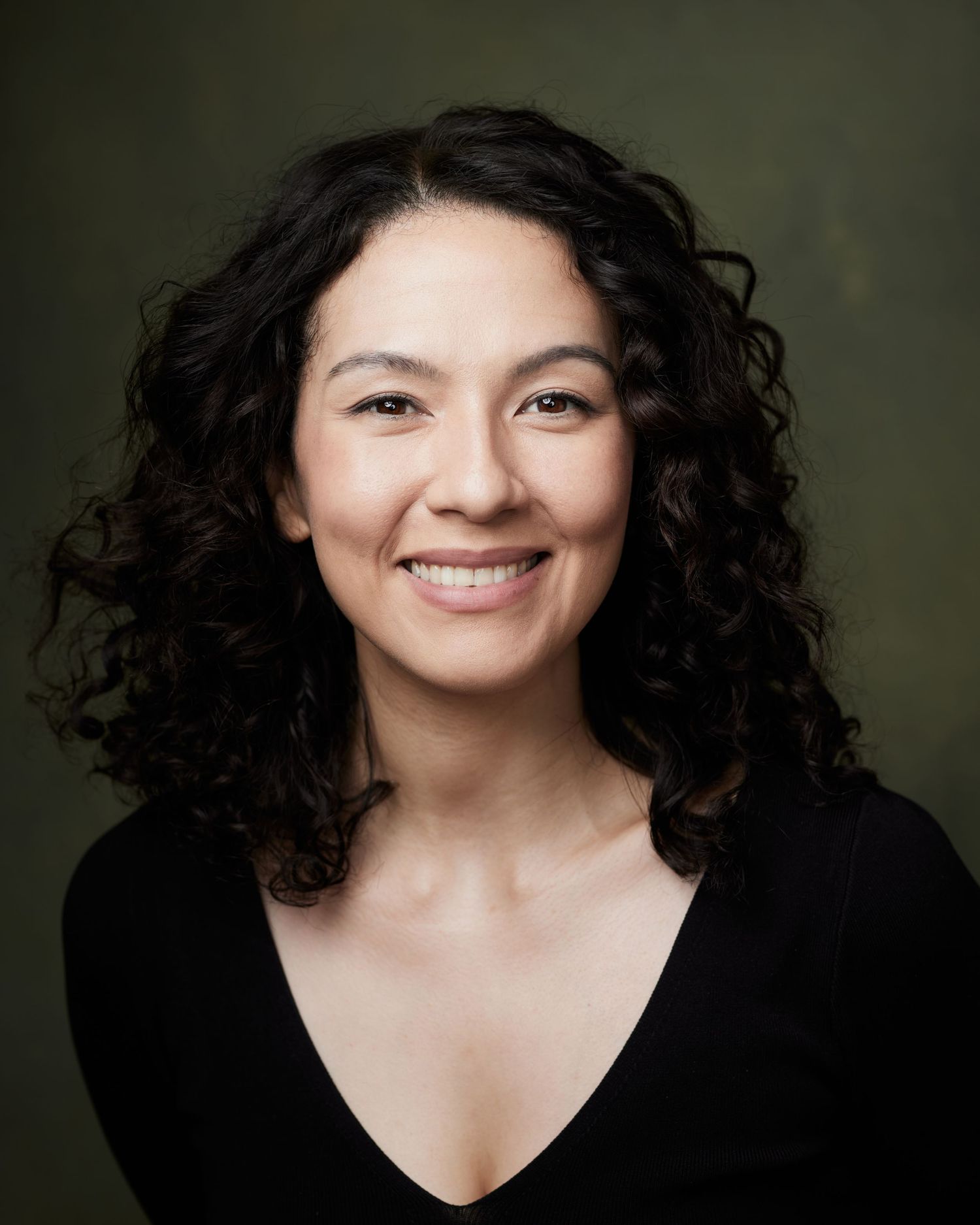 Actor headshot of a female performer with warm eyes and a big smile on a green backdrop.