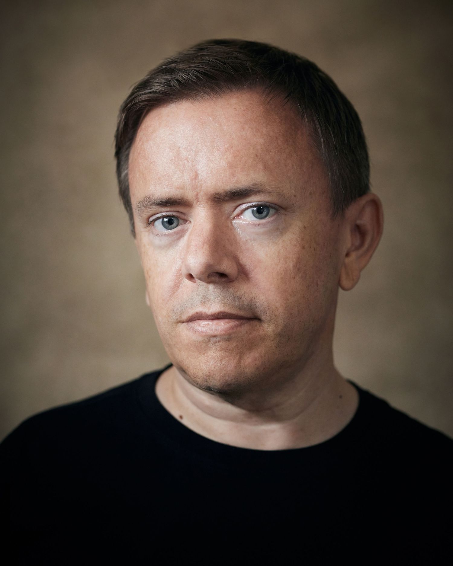 Commanding studio portrait; actor with a focused, serious look against a brown canvas backdrop.