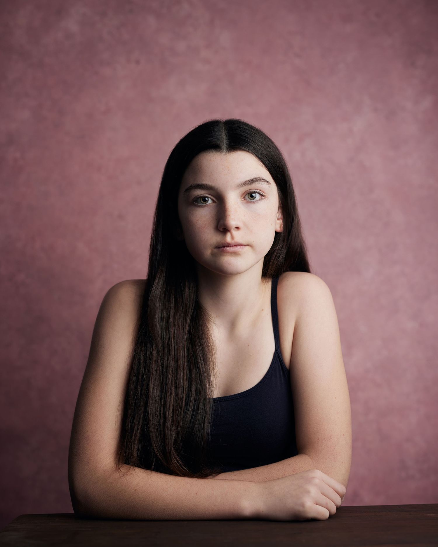 Serious studio light portrait; child actress with a strong presence and direct eye contact against a pink background.