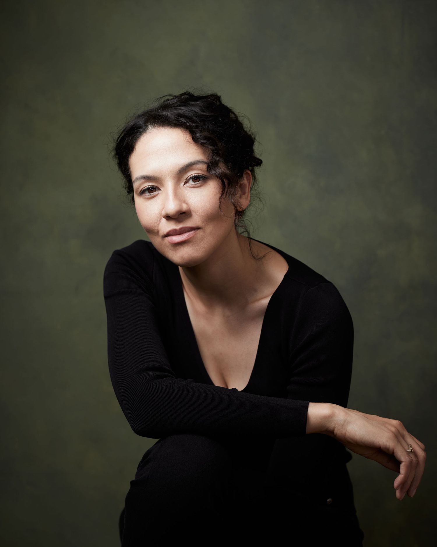 Powerful studio headshot; actress with a sharp, ambitious confidence against a green canvas backdrop.
