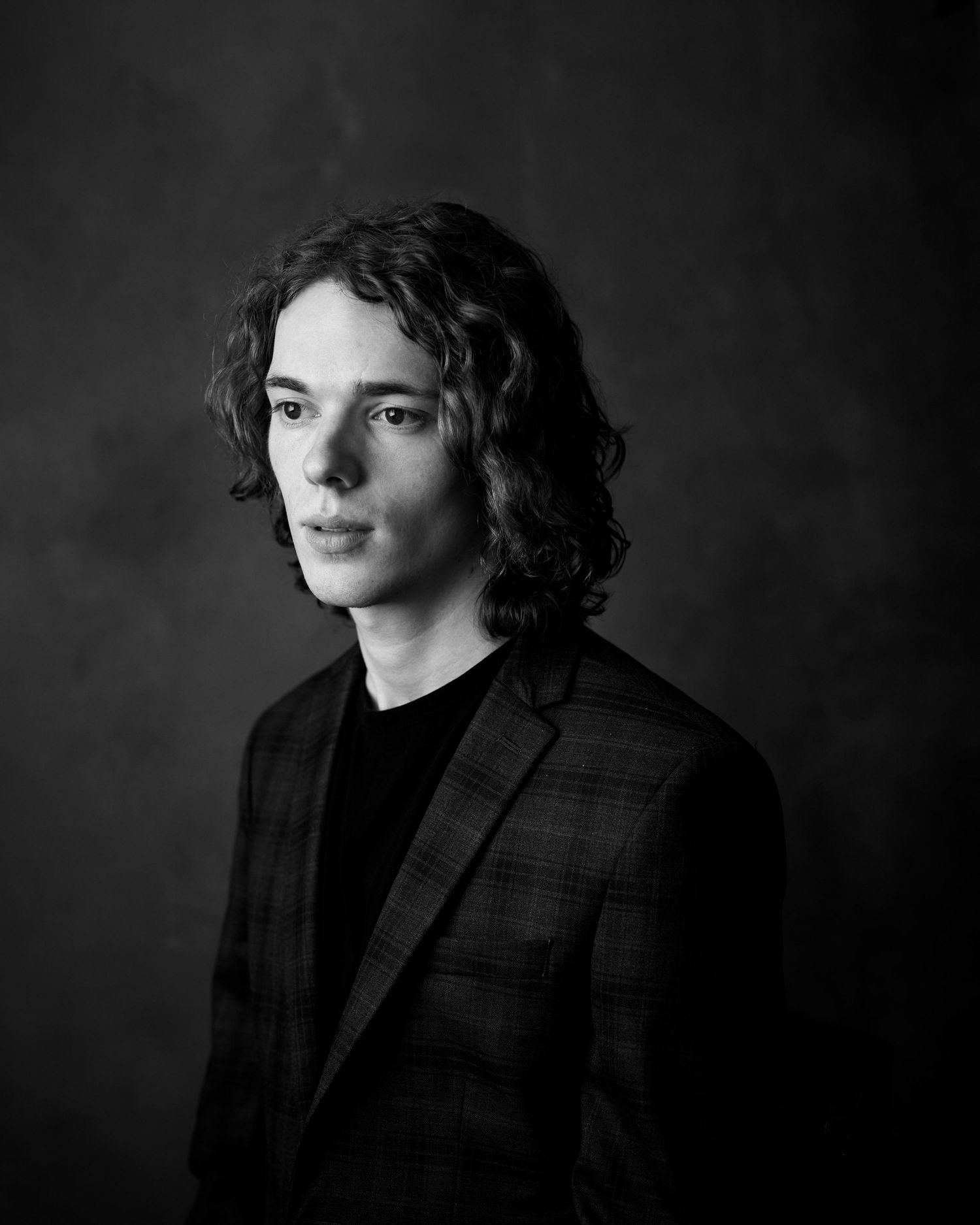 Black and white cinematic headshot of an actor with long curly hair, wearing a textured blazer against a dark background in Cardiff.