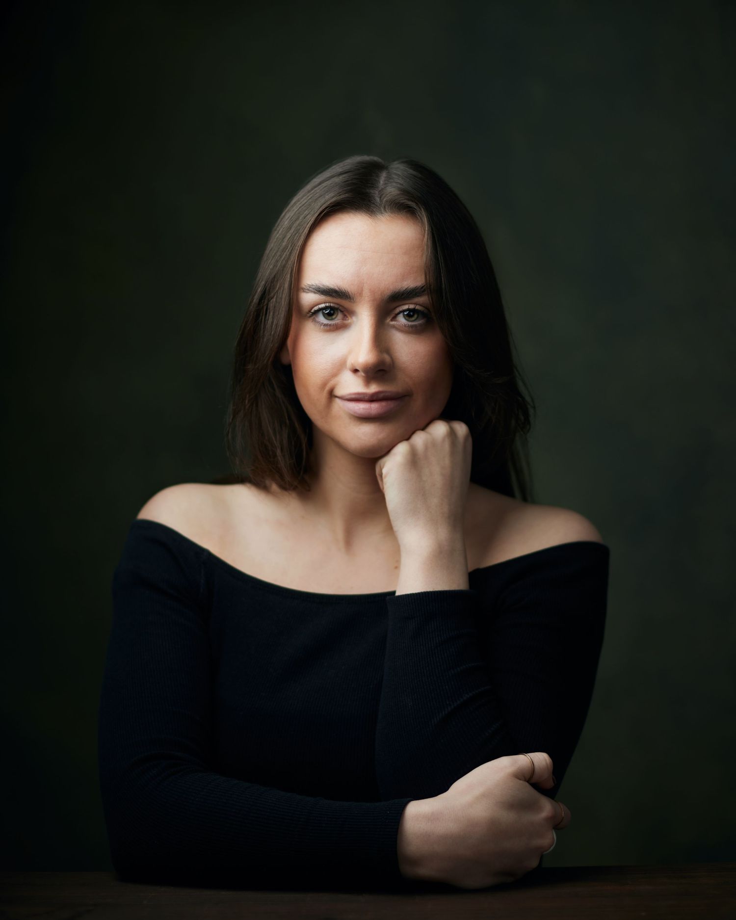 Cinematic headshot; female performer with a mysterious, guarded look on a sage green background.