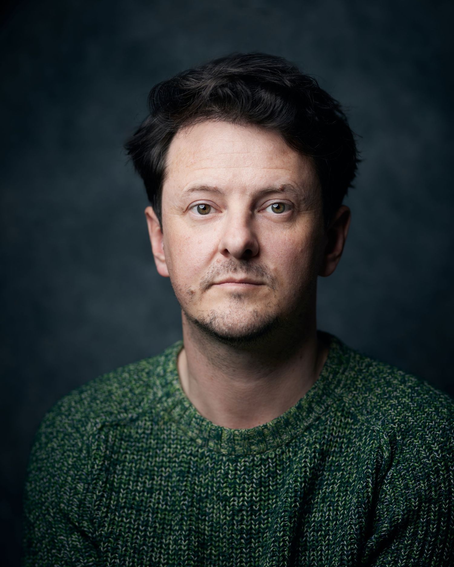 Calm studio headshot; man with a natural expression and strong eye contact under studio lighting.
