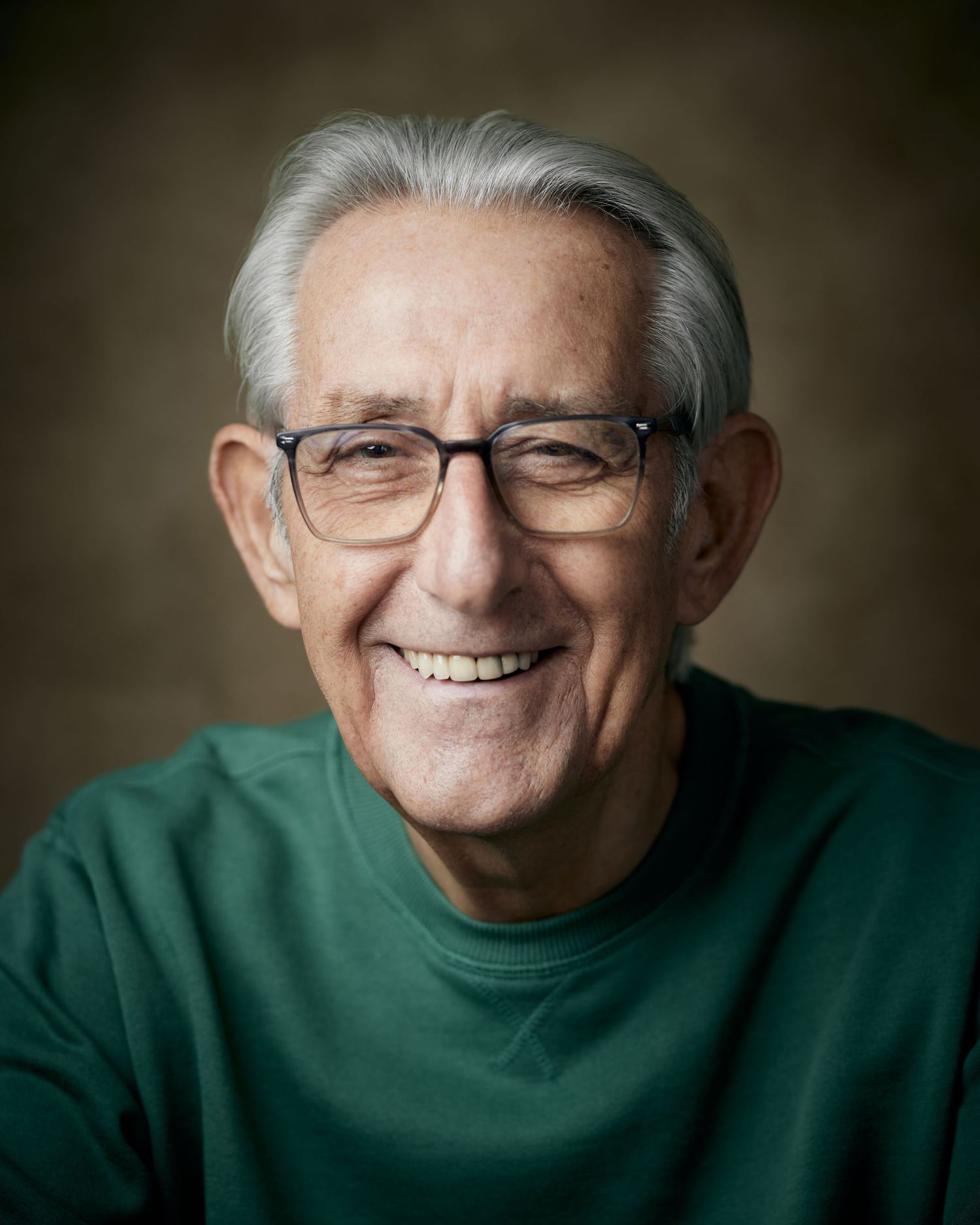 A smiling actor headshot of a man wearing glasses with a genuine warm smile.