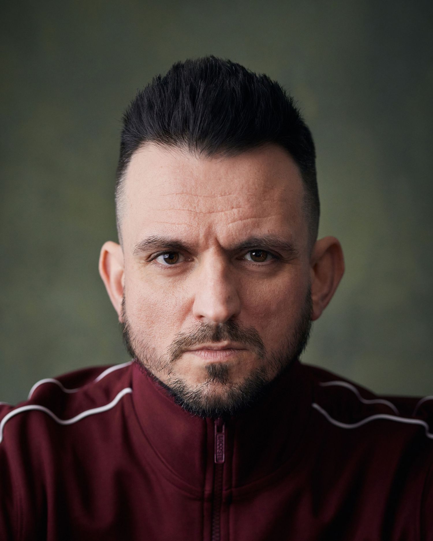Strong actor headshot; man with a piercing, intense gaze and dramatic studio lighting against a green canvas backdrop.