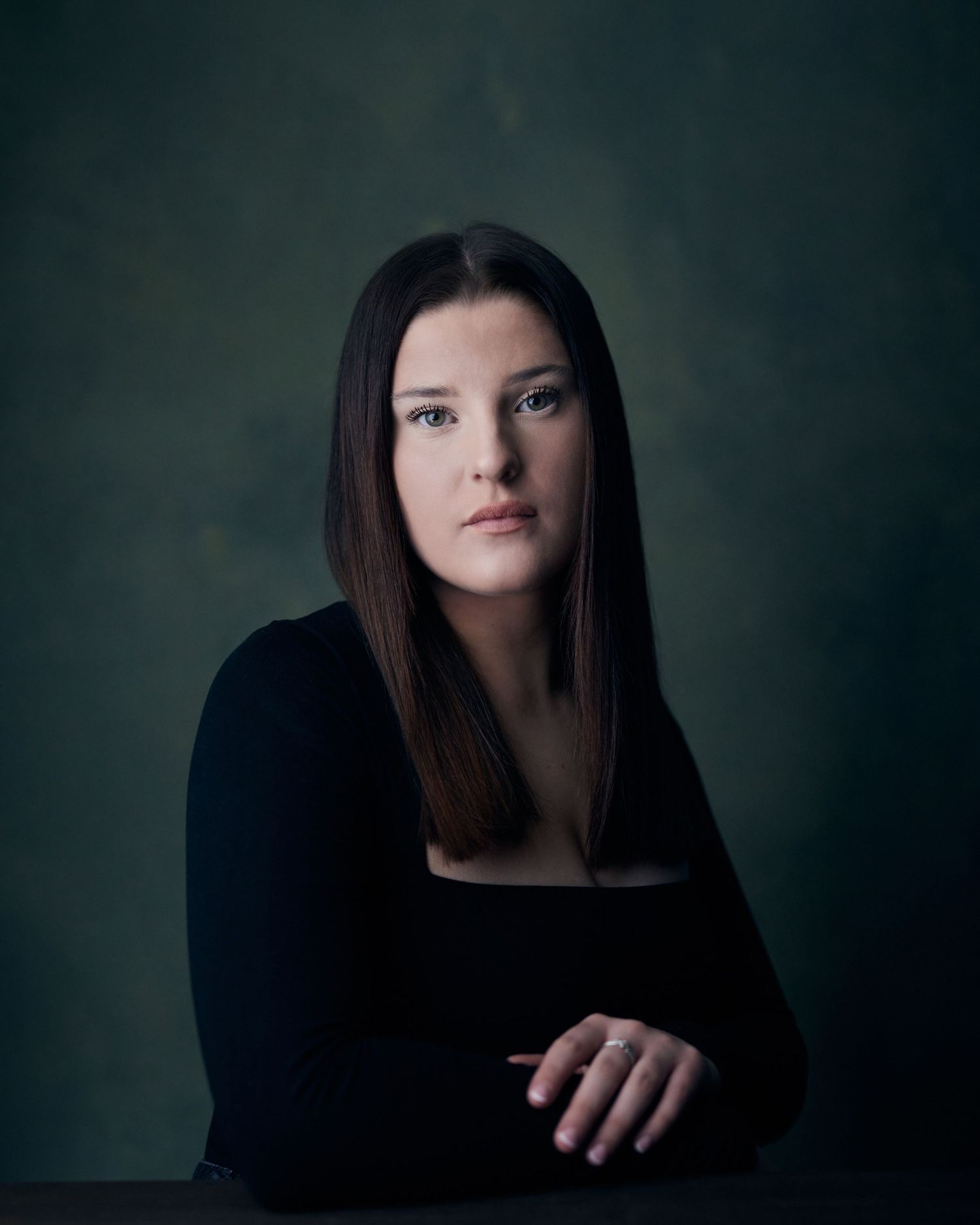 Dramatic actor headshot; woman with a piercing, serious gaze against a dark green textured backdrop.