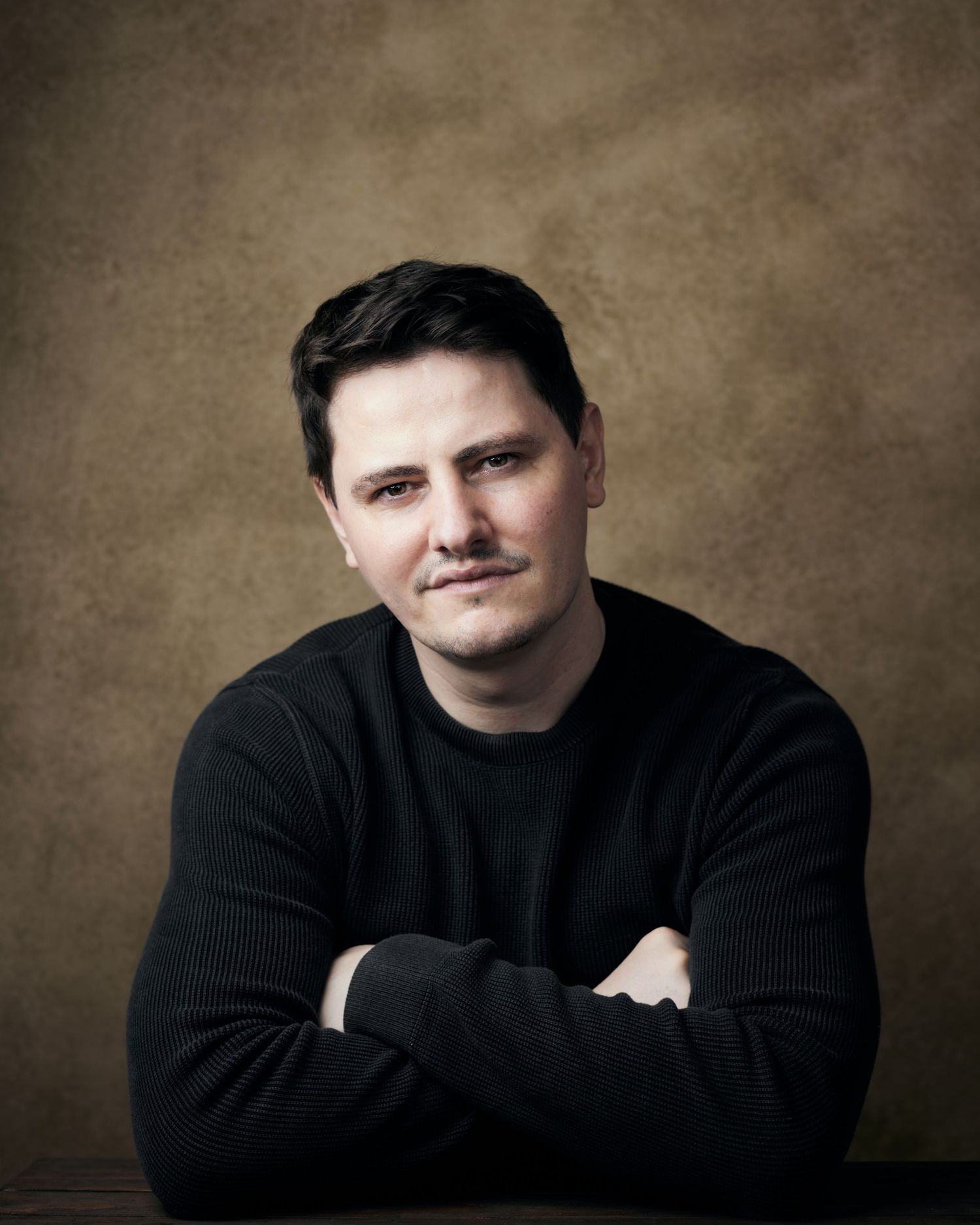 Powerful studio portrait; actor with a stoic, commanding presence against a brown canvas backdrop.