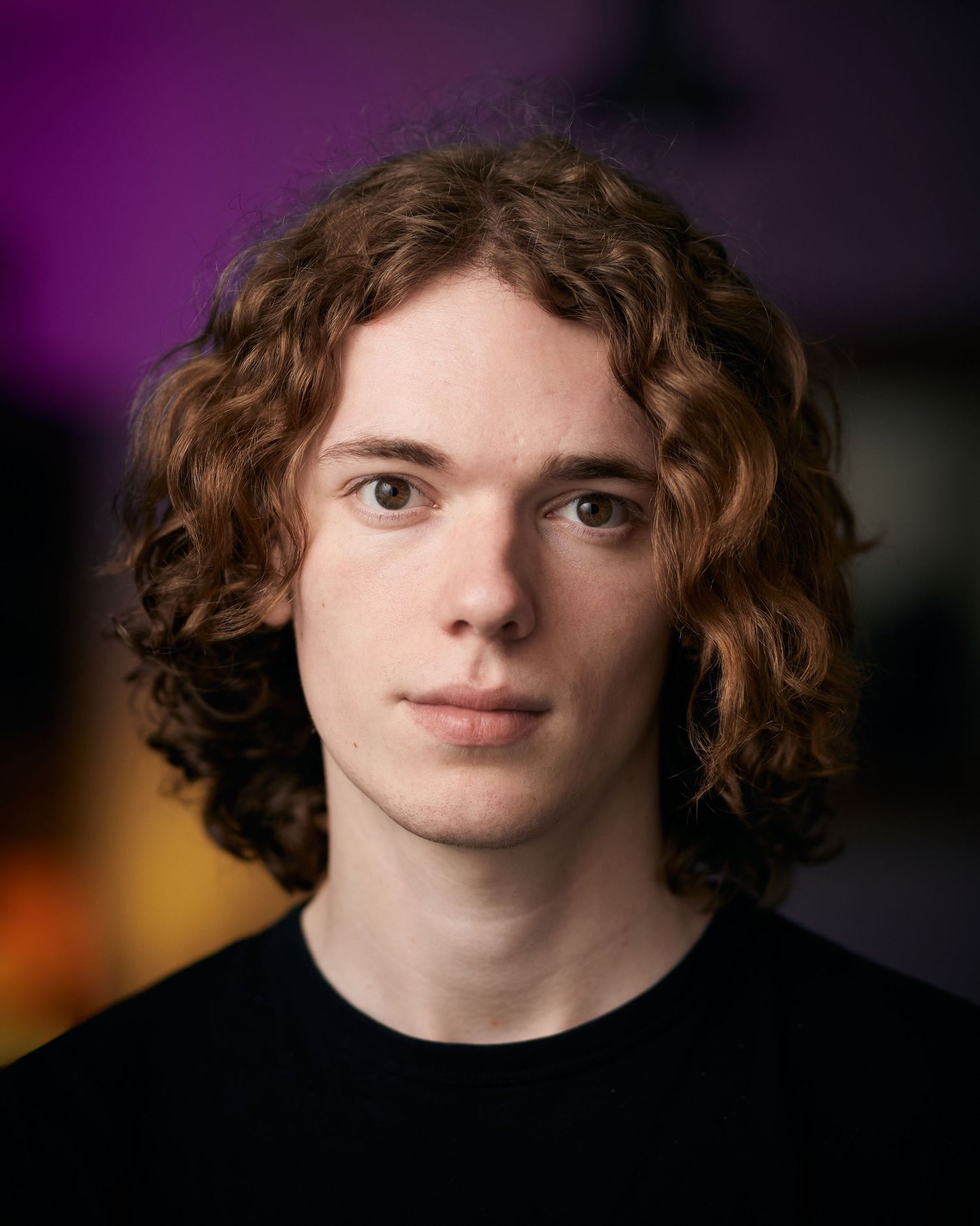 Actor headshot of a man with curly hair against a vibrant purple and yellow background by Cardiff photographer Geraint Todd.