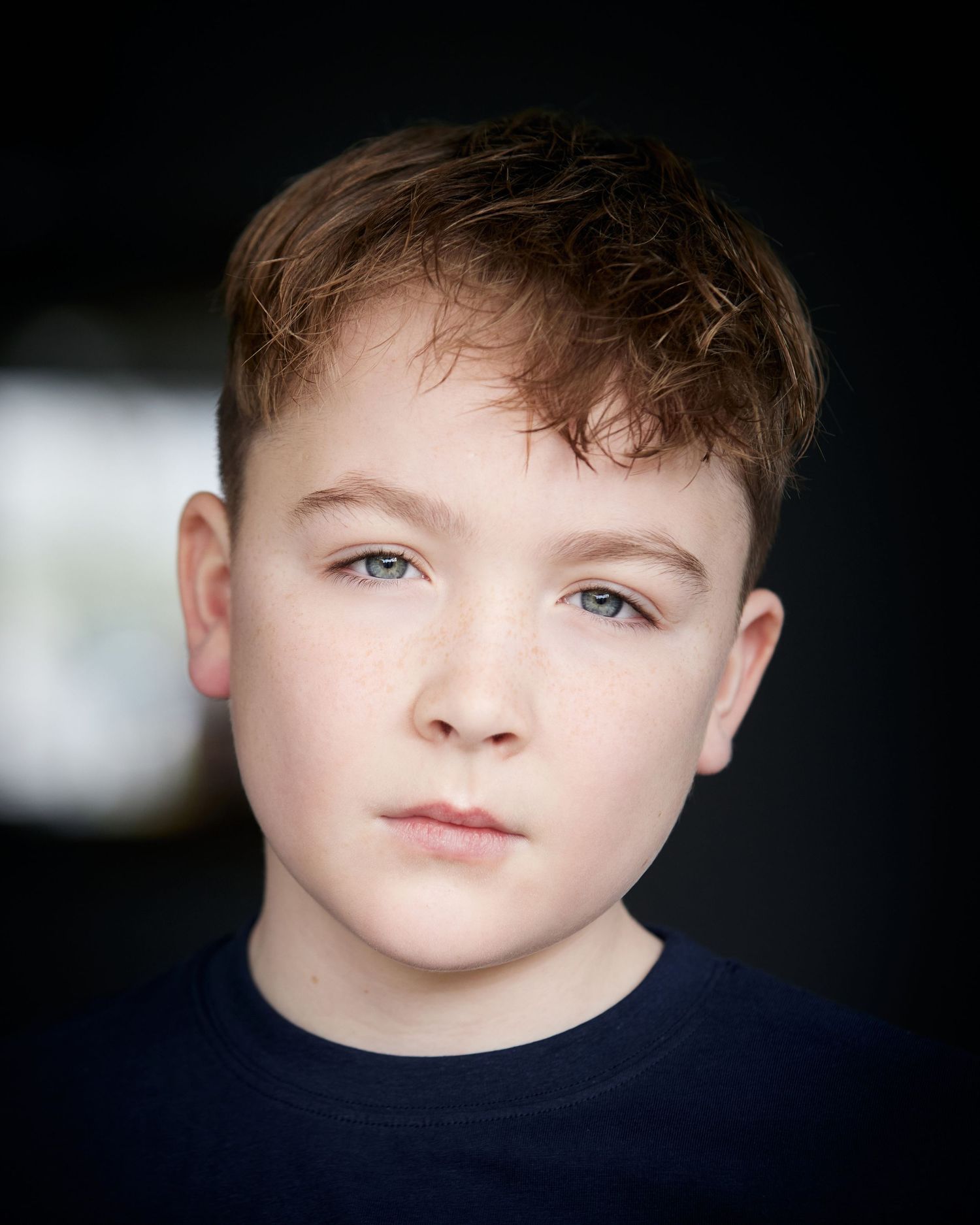 Serious natural light portrait; child actor with a grounded, defiant  presence and blurred background.