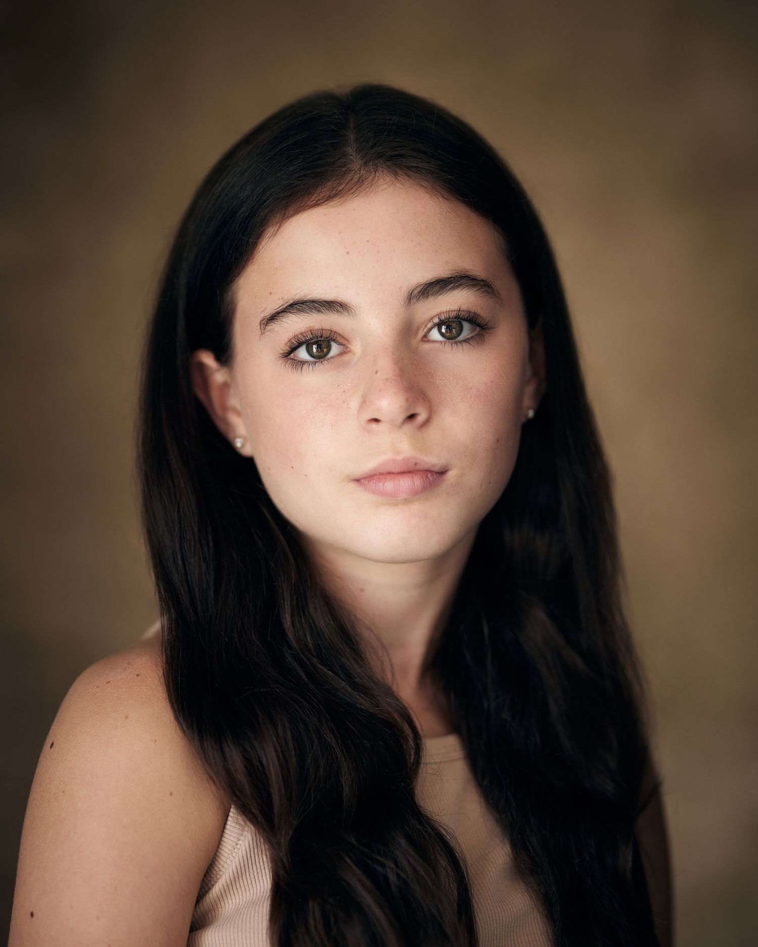Professional child actor portrait; girl with a confident, polished gaze on brown.