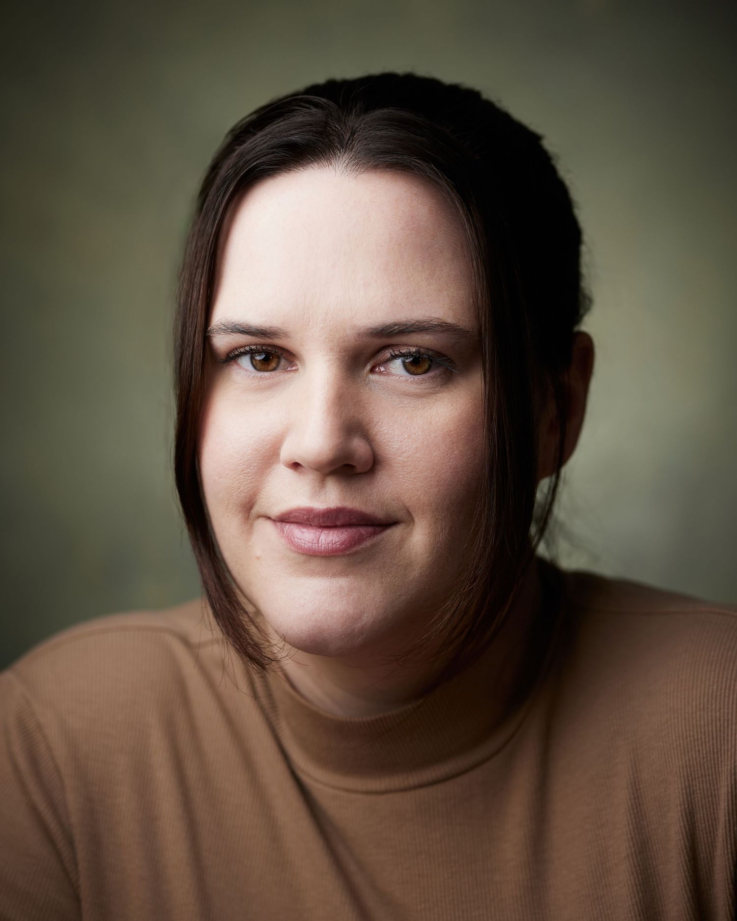 Engaging studio portrait of an actress leaning forward with a friendly expression on a green background.