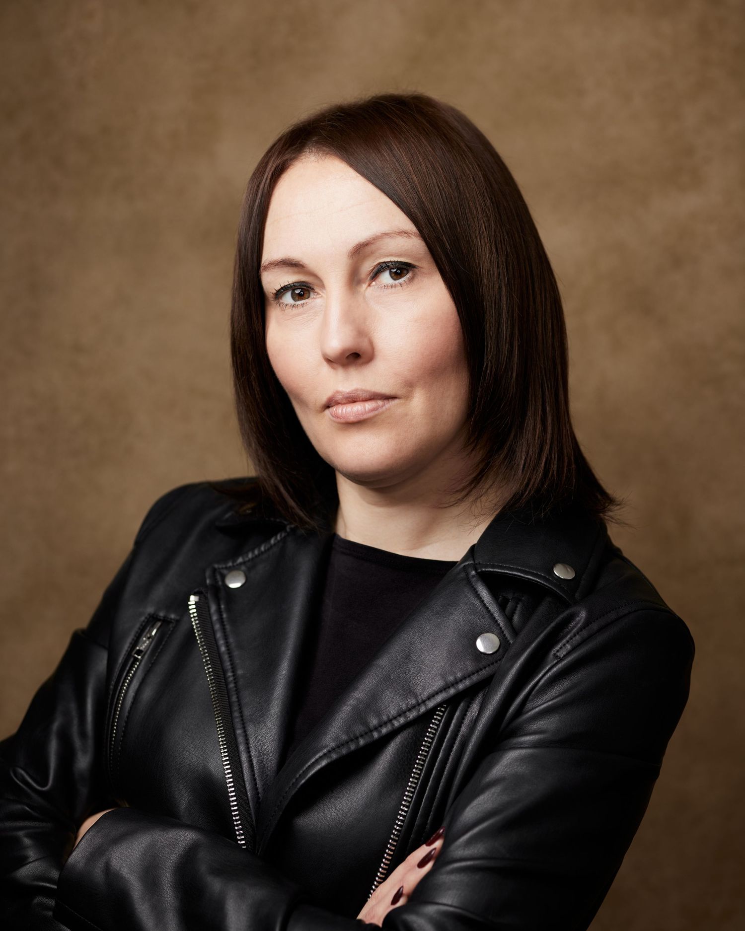 Modern studio portrait; female actor with a defiant look and sharp lighting against a brown canvas backdrop.