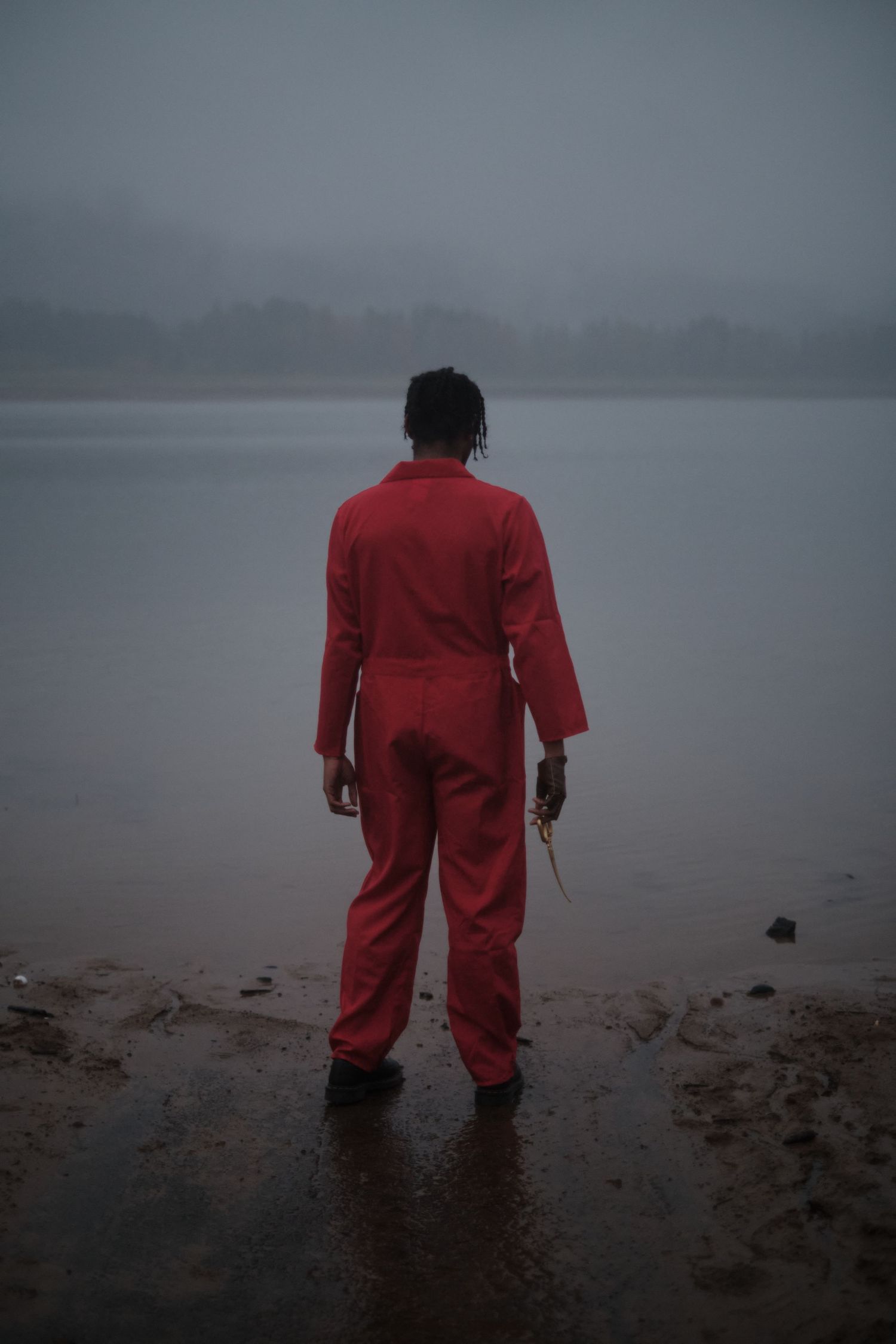Silhouette of person in red coveralls standing in misty water.