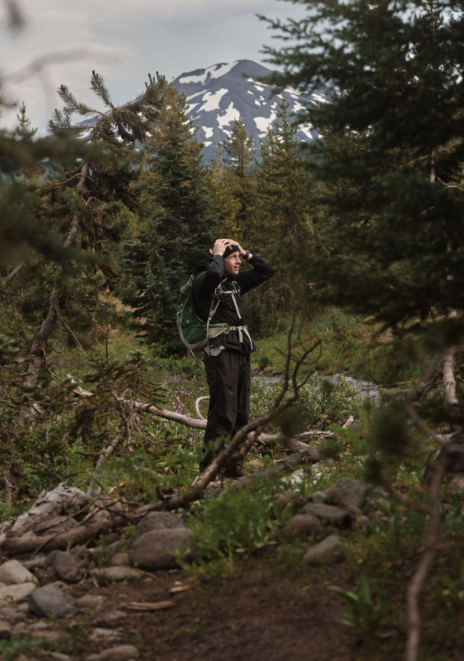 A person in dark clothing explores a rocky mountain trail surrounded by evergreen trees.