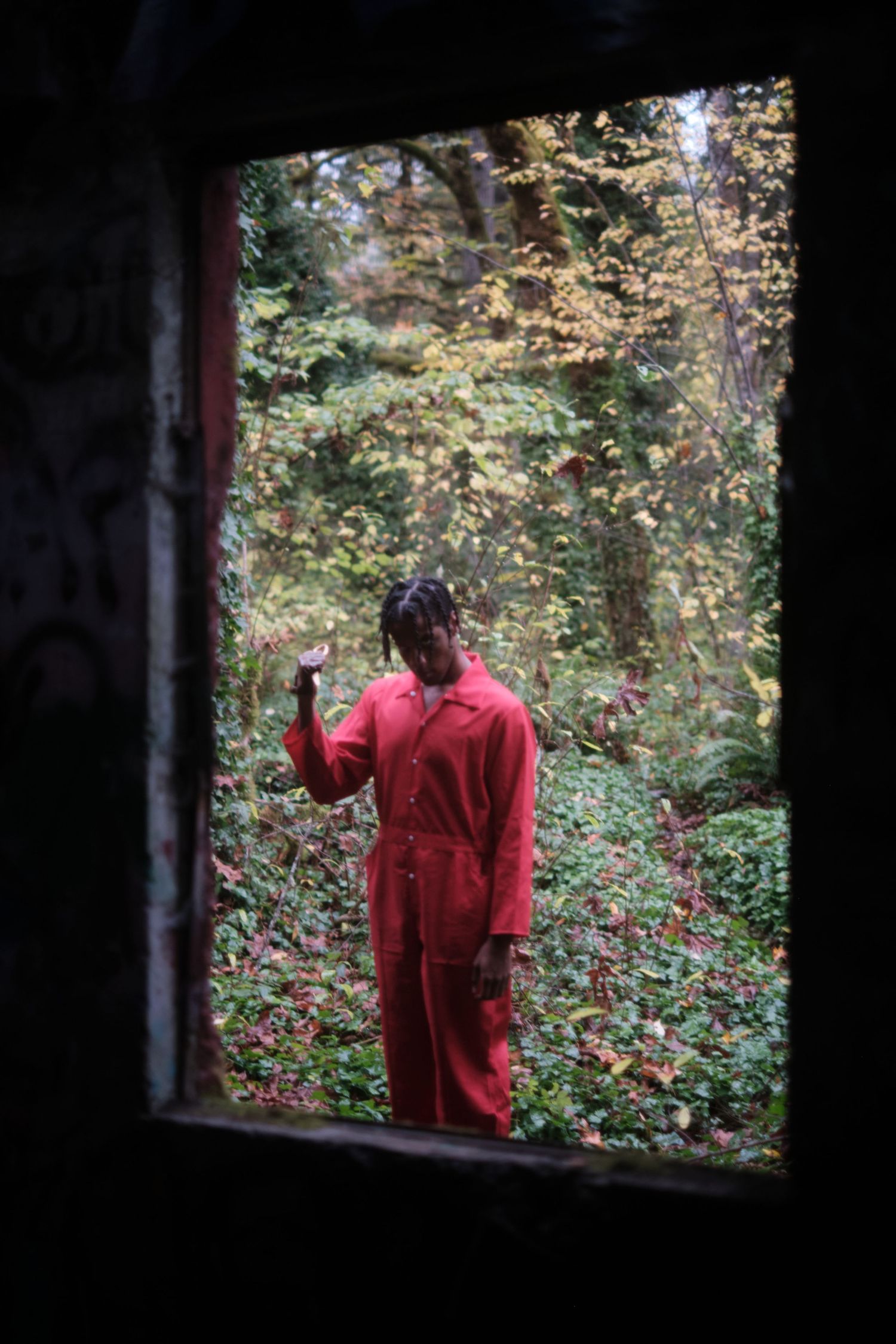 Figure in red clothing viewed through window frame surrounded by autumn foliage.