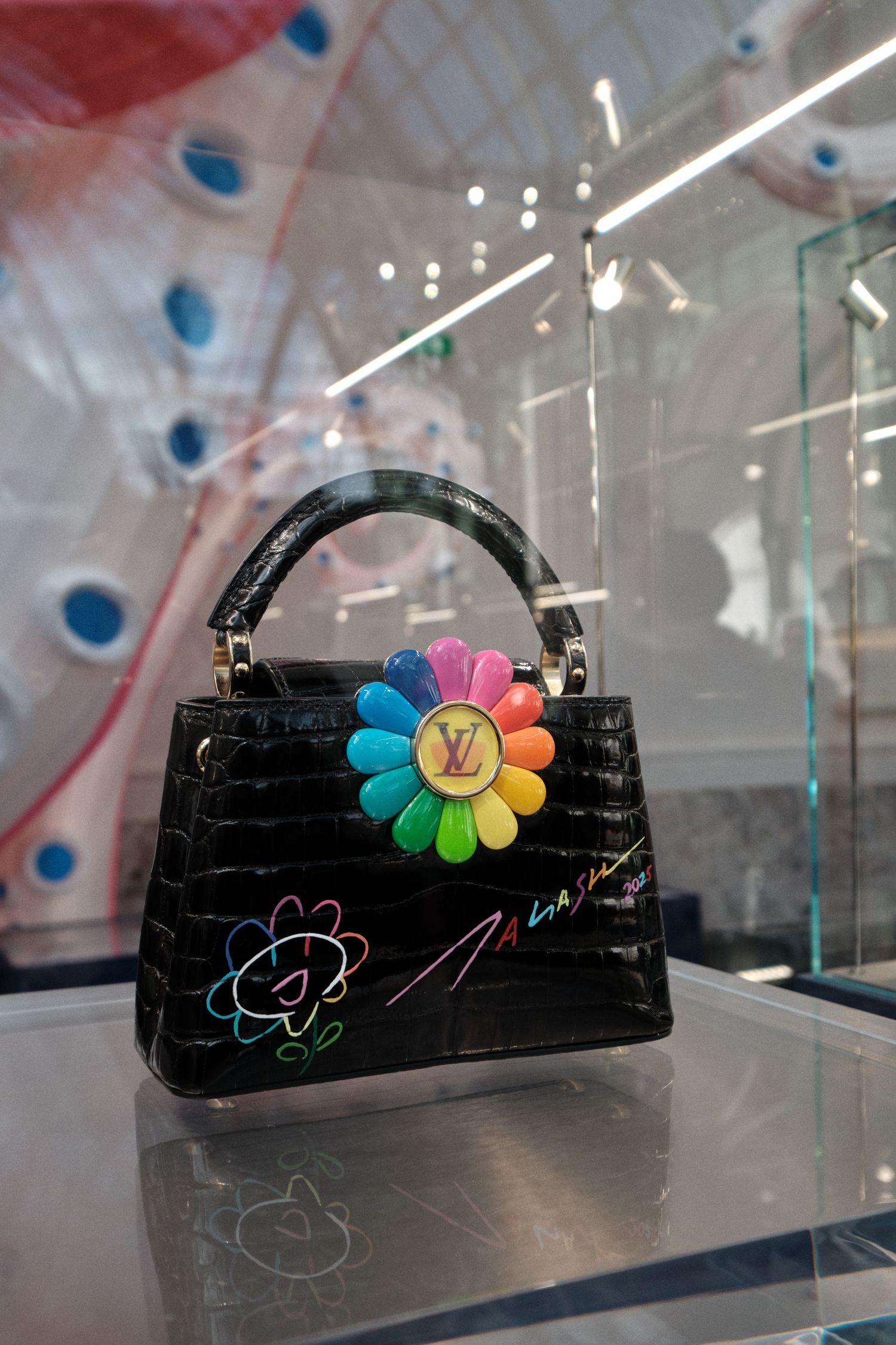 Black Louis Vuitton handbag decorated with colorful flower embellishments displayed in glass case.