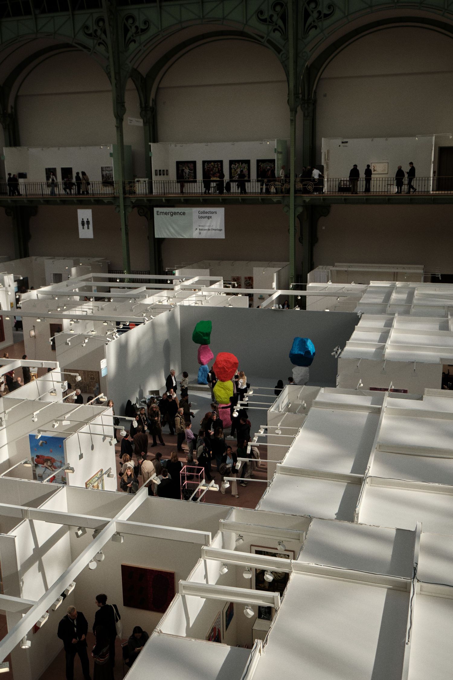Art fair venue with white exhibition booths and visitors exploring the space.