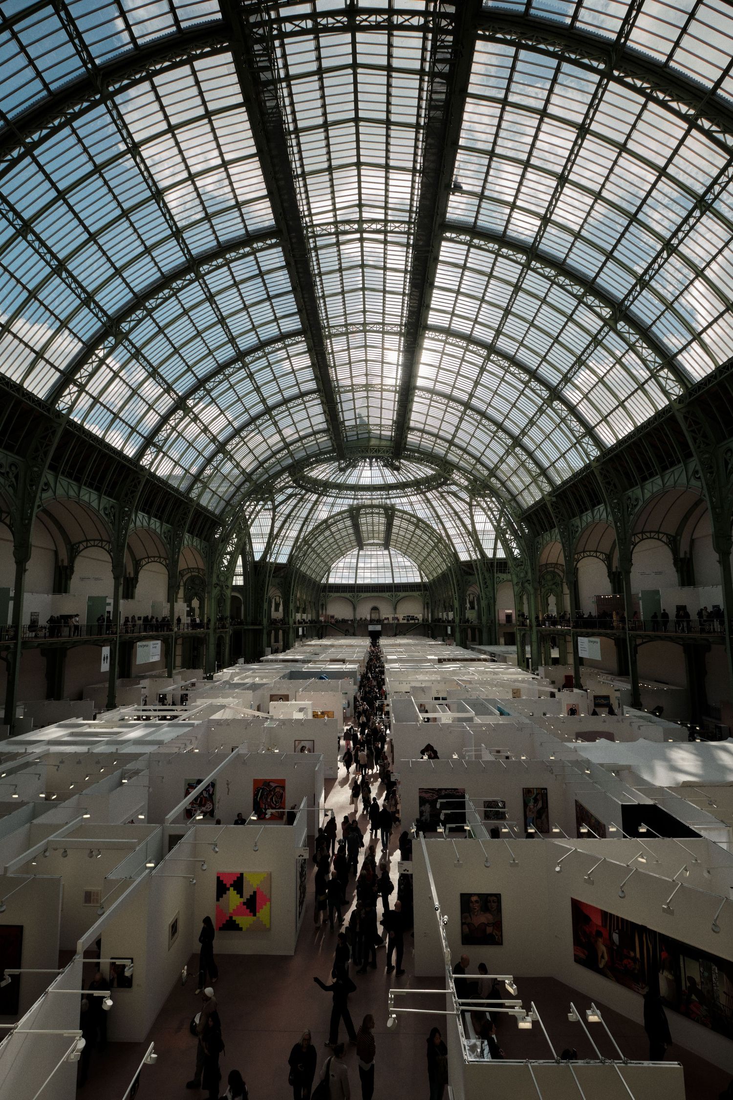 Grand exhibition hall with glass ceiling and white display booths arranged in asymmetrical rows.