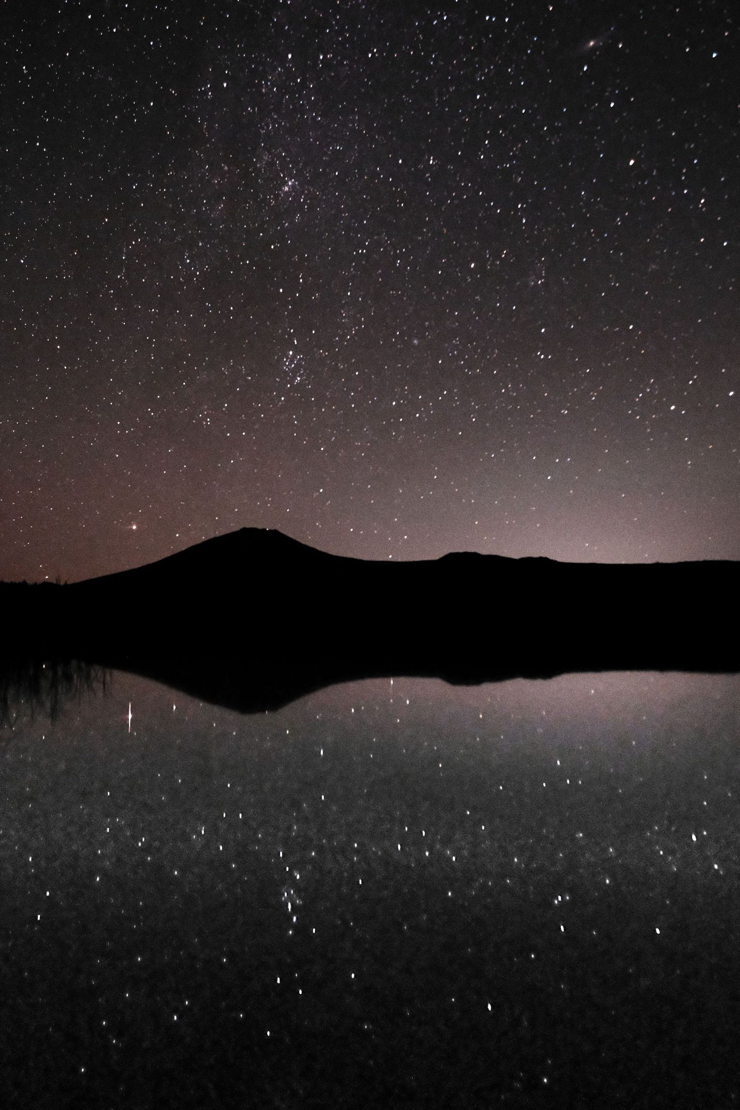 Stars twinkle in the dark sky above mountain silhouettes at night.