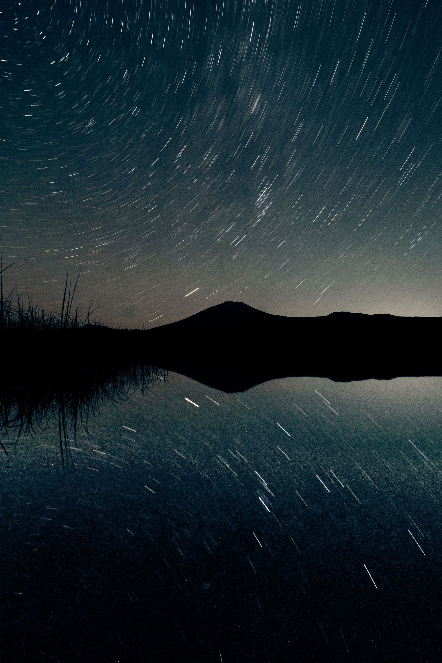 Star trails streak across the night sky above a silhouetted mountain range.