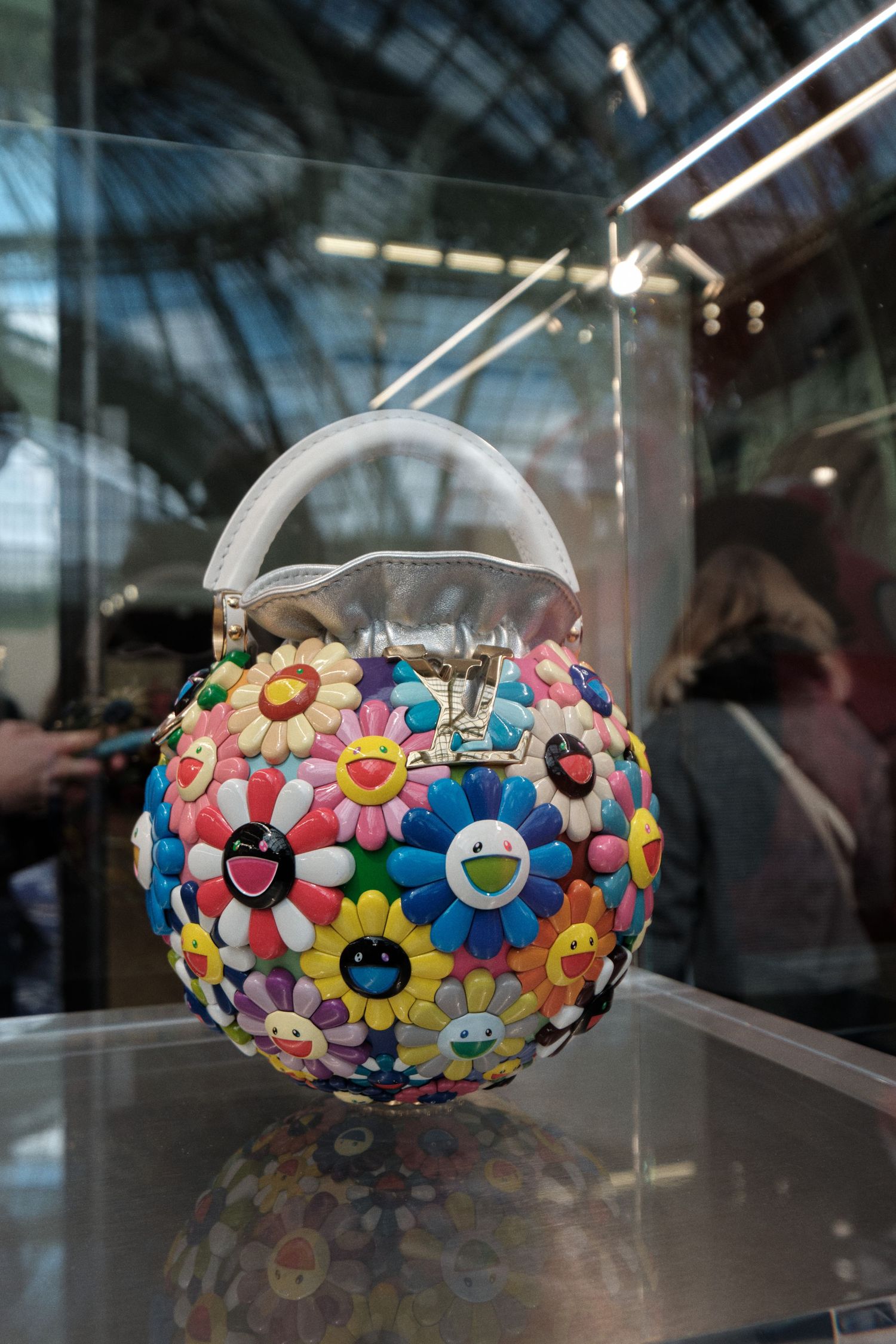 Colorful Louis Vuitton handbag decorated with playful flower and smiley face designs in display case.