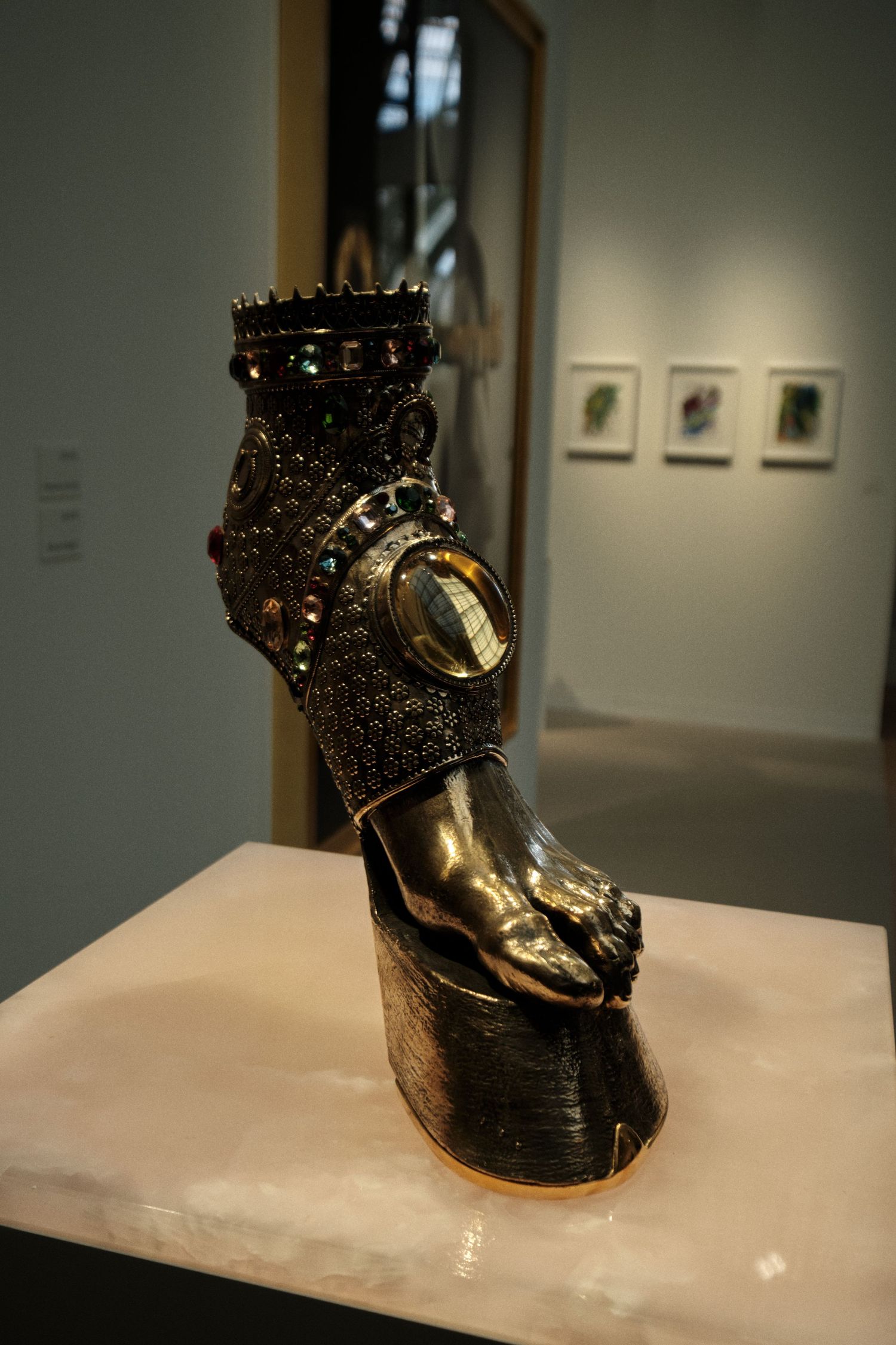 Bronze sculptural foot with ornate crown-like details displayed on museum pedestal.