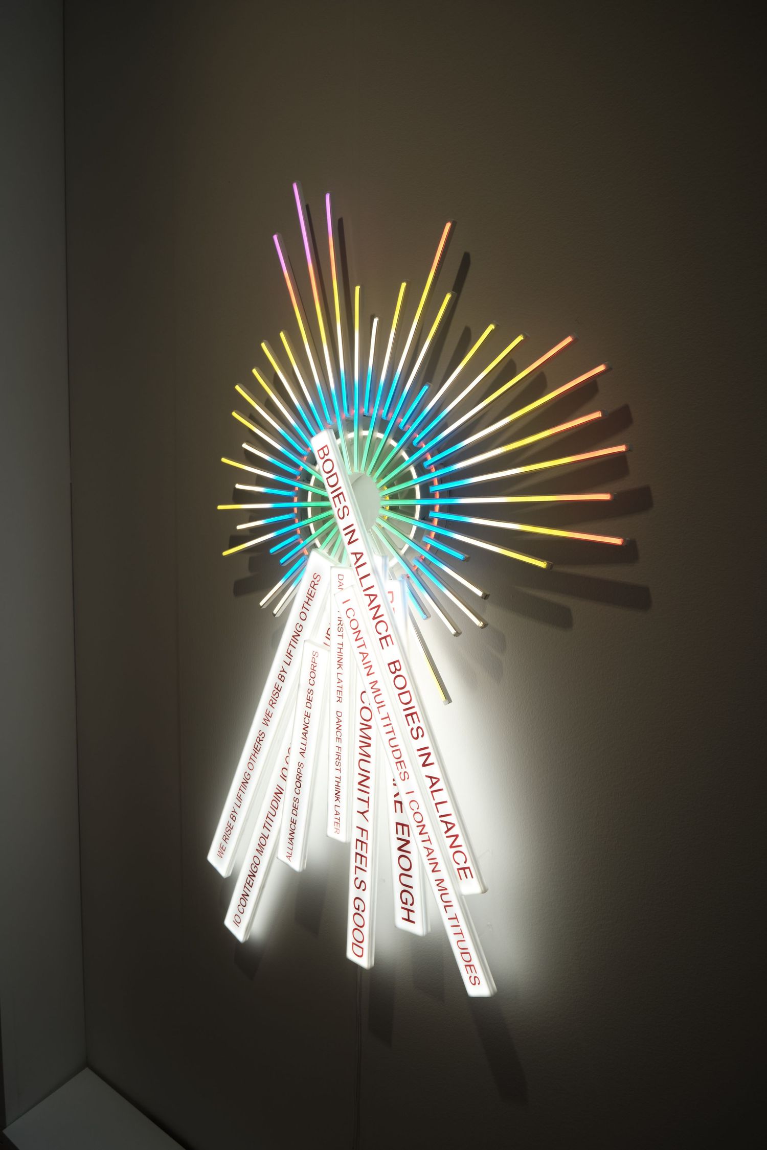 Illuminated art installation with colorful neon rays radiating from central white text.