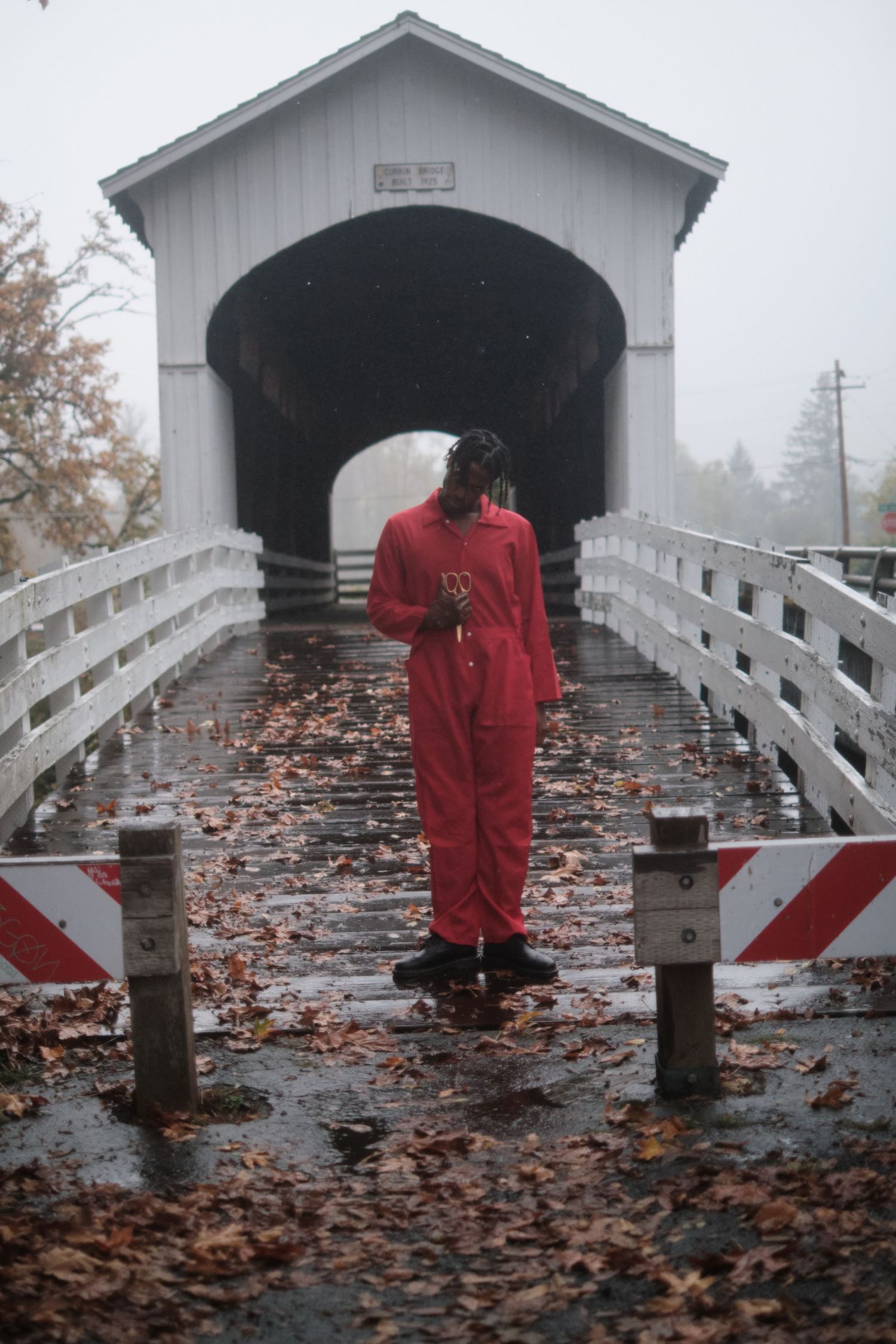 Person in red coveralls walks through a covered bridge filled with fallen leaves.
