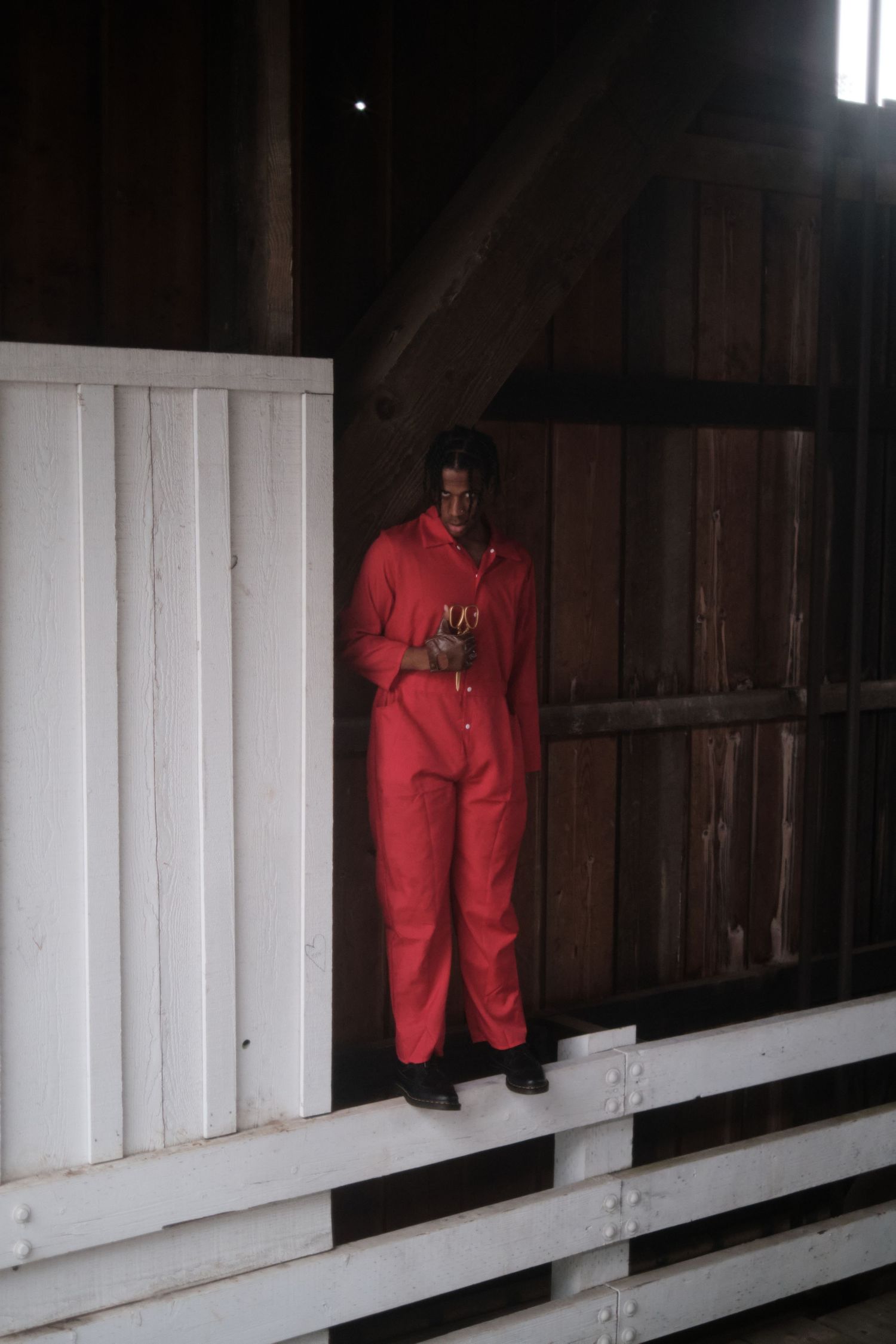 Someone wearing red stands in a dimly lit wooden corridor.