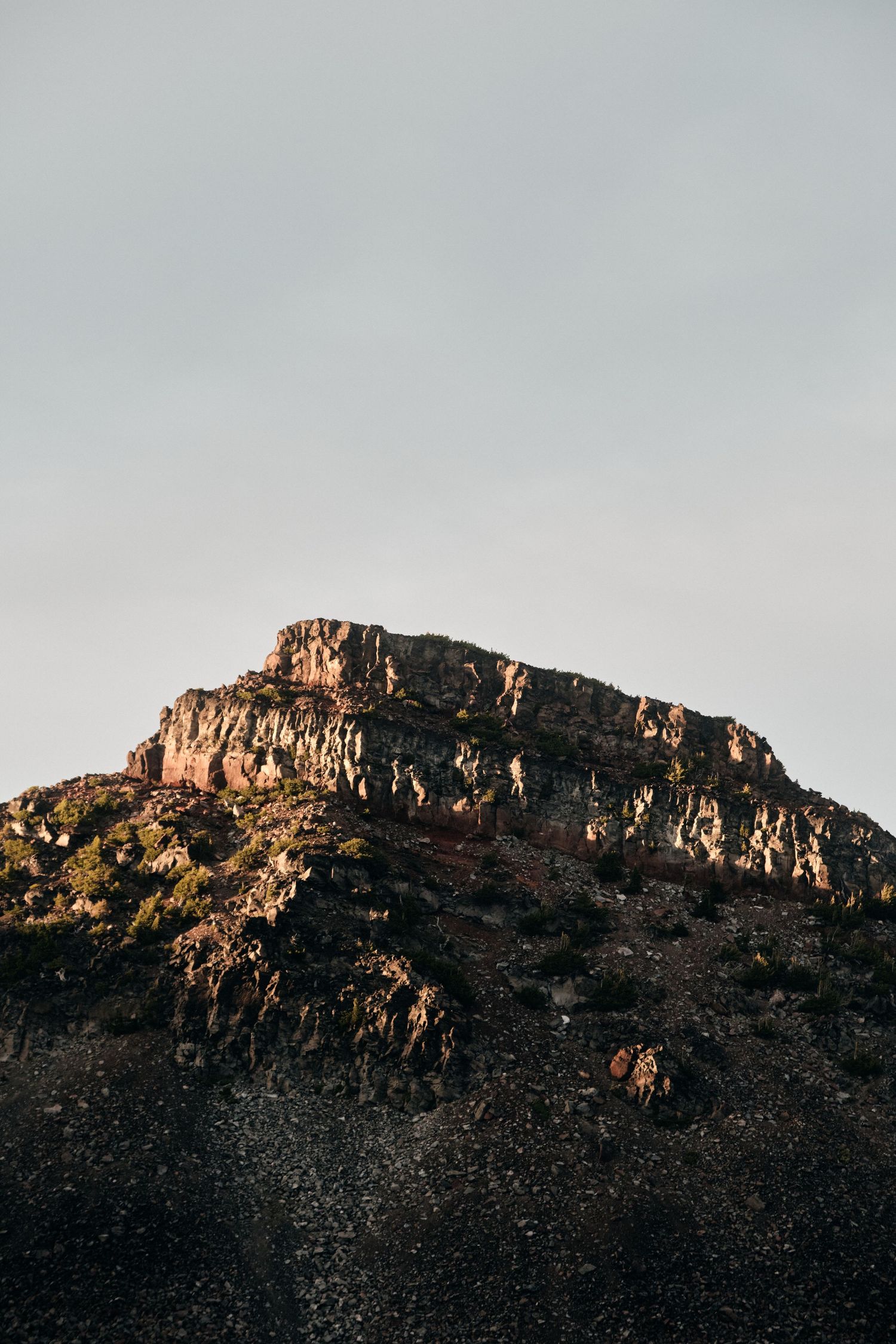Rocky mountain ridge glowing golden in evening light against clear sky.