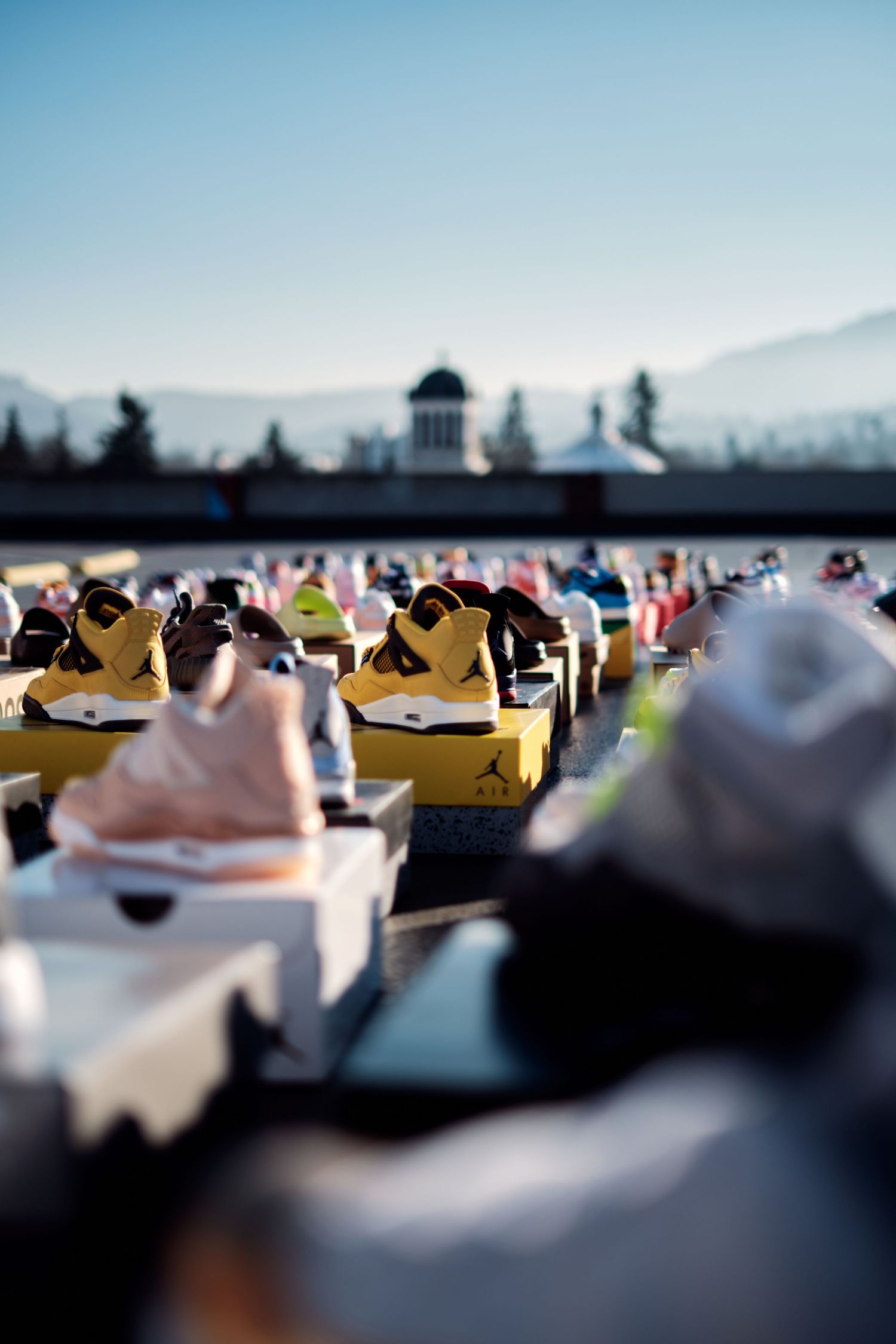 Collection of sneakers arranged in rows outdoors against blue sky and mountain backdrop.