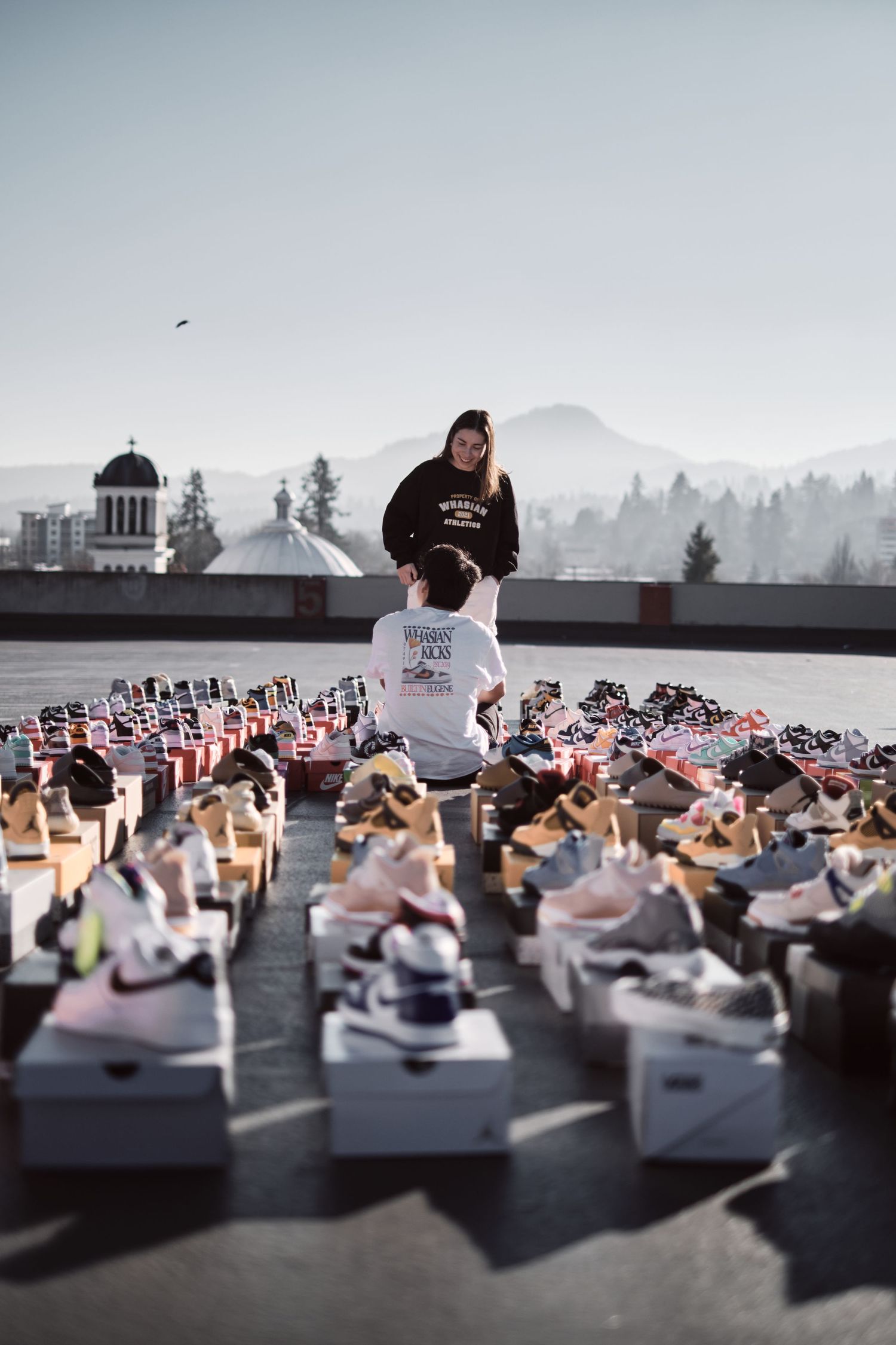 Multiple pairs of sneakers arranged in rows on a dark rooftop with mountains visible in the background.