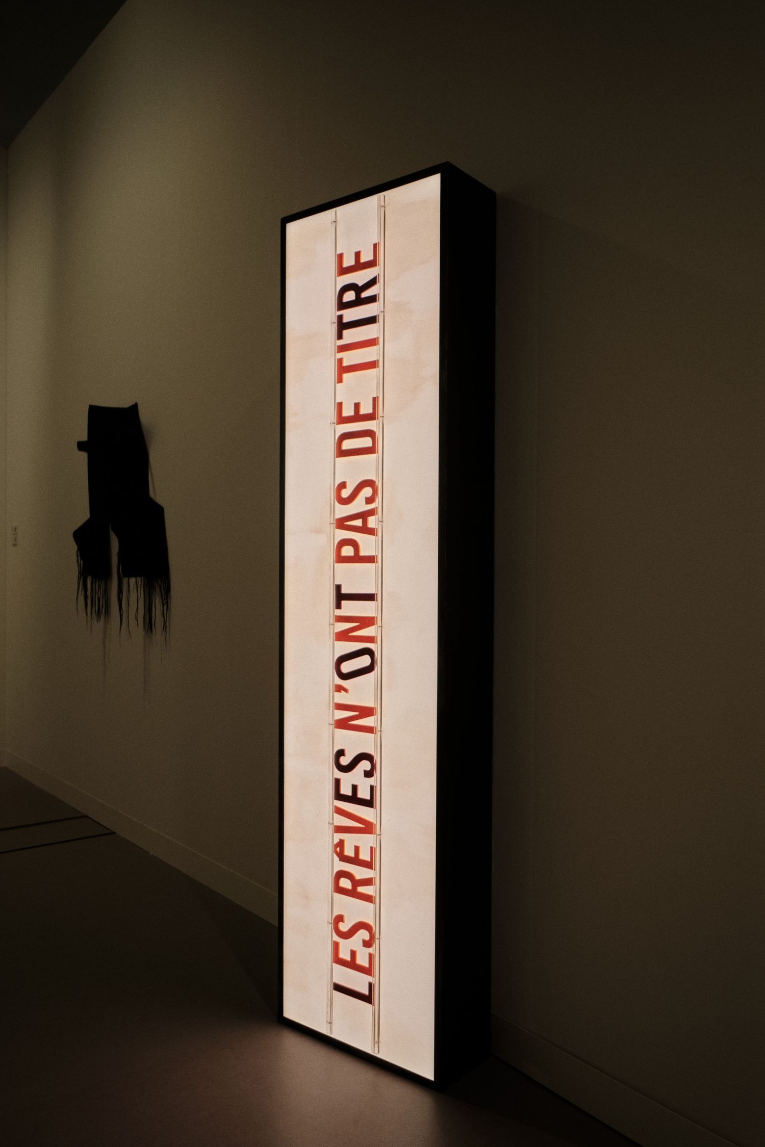 Illuminated text art installation in dark gallery space with red lettering.