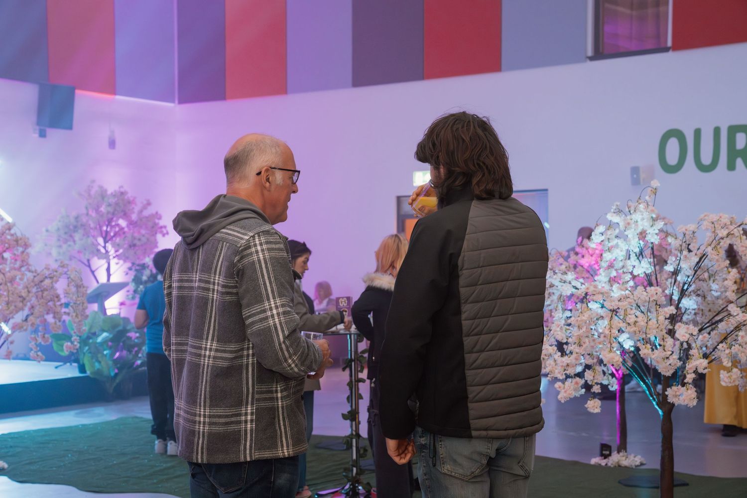 People gather around illuminated cherry blossom trees at a colorful indoor event display.